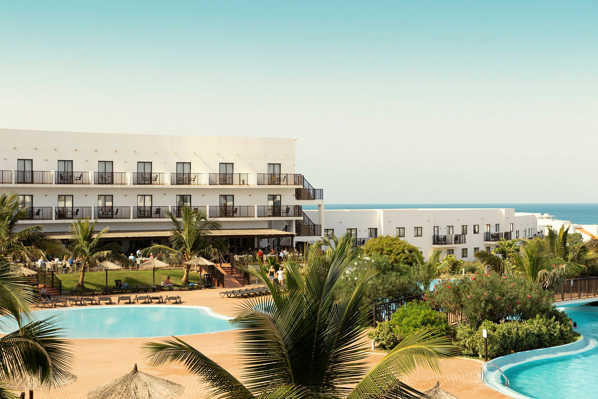 Hotelbygning ved en pool og grønt område. (AI-genereret tekst)