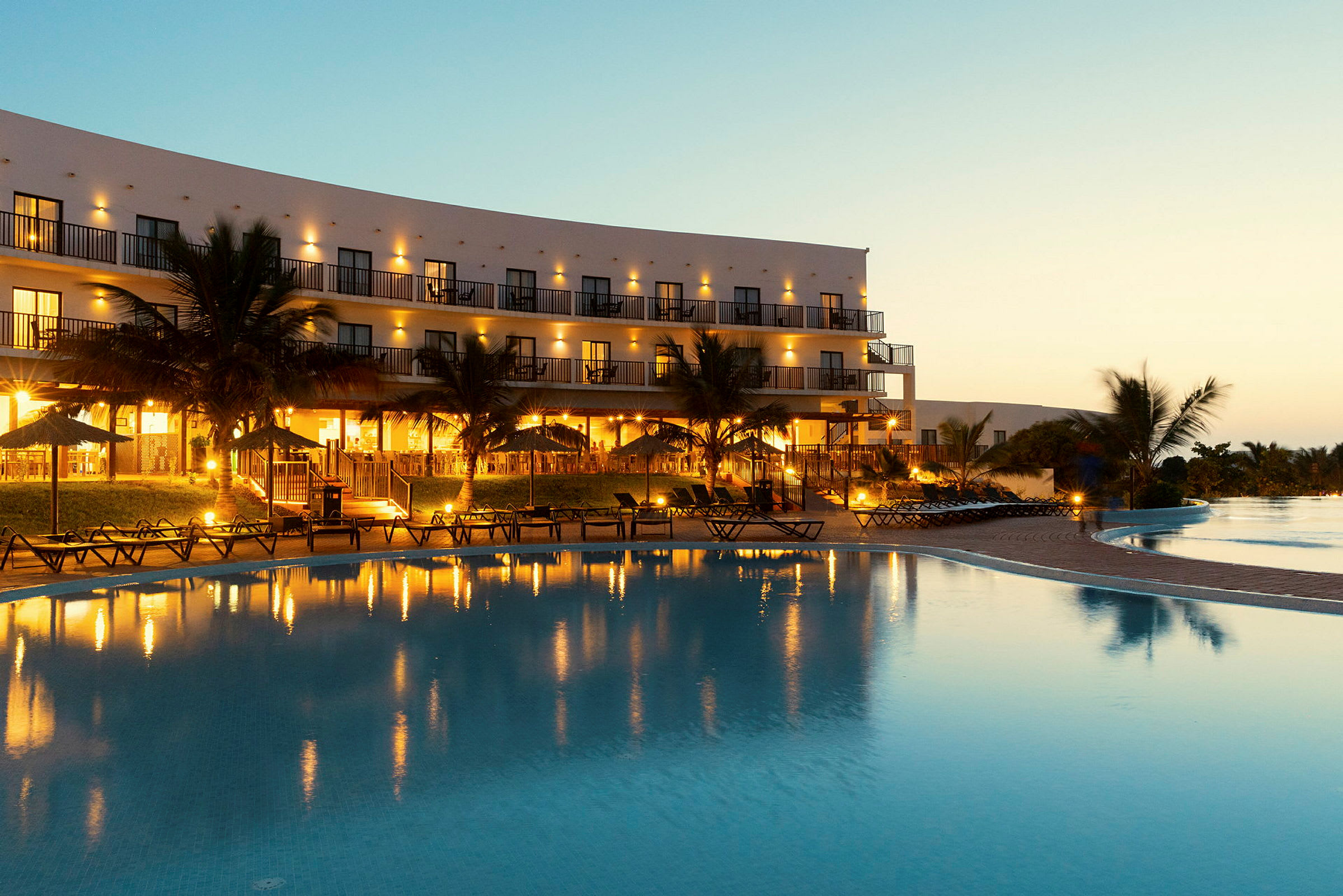 En oplyst hotelbygning ved en stor swimmingpool ved skumring. (AI-genereret tekst)
