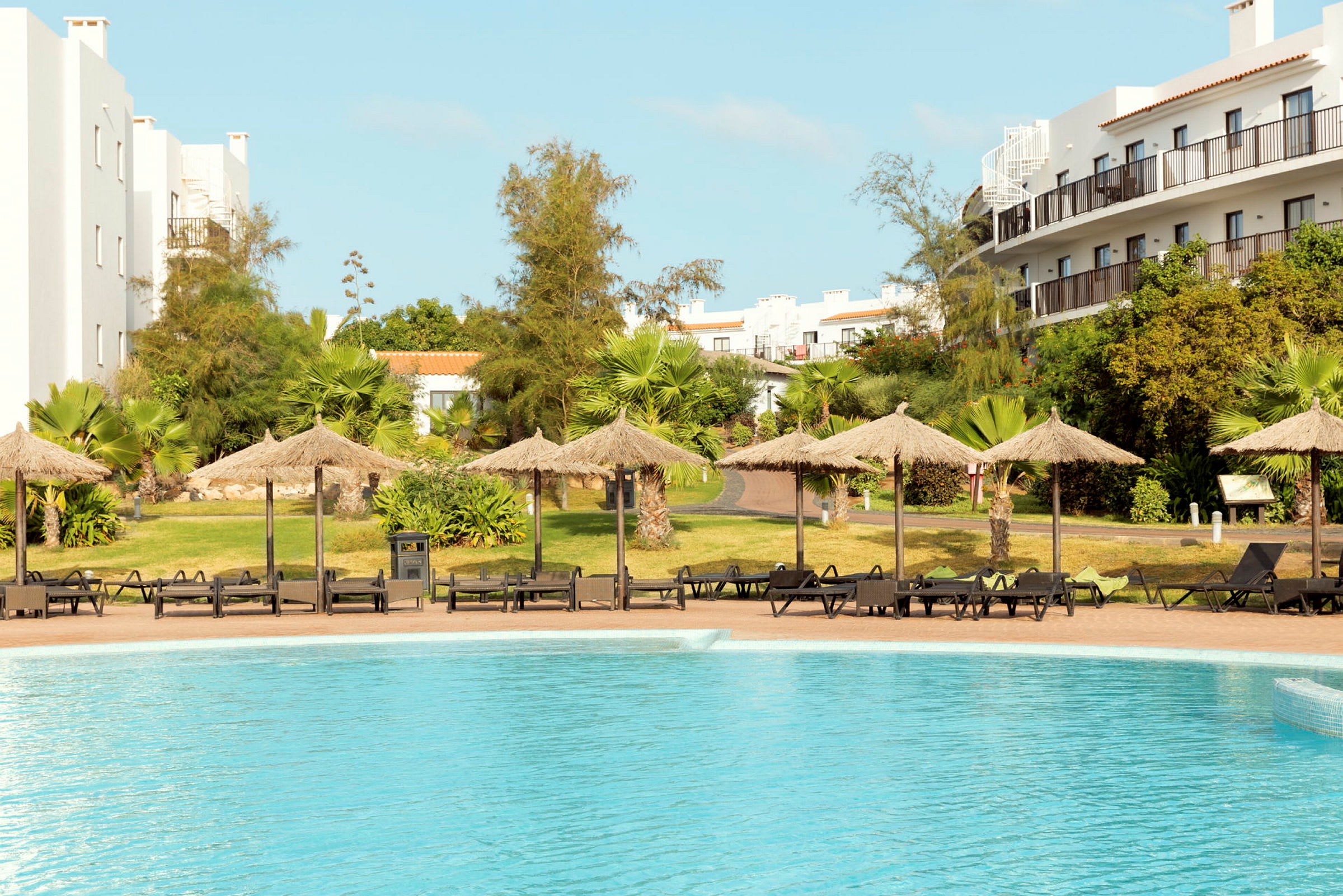 Pool med parasoller og liggestole ved hotelområdet. (AI-genereret tekst)