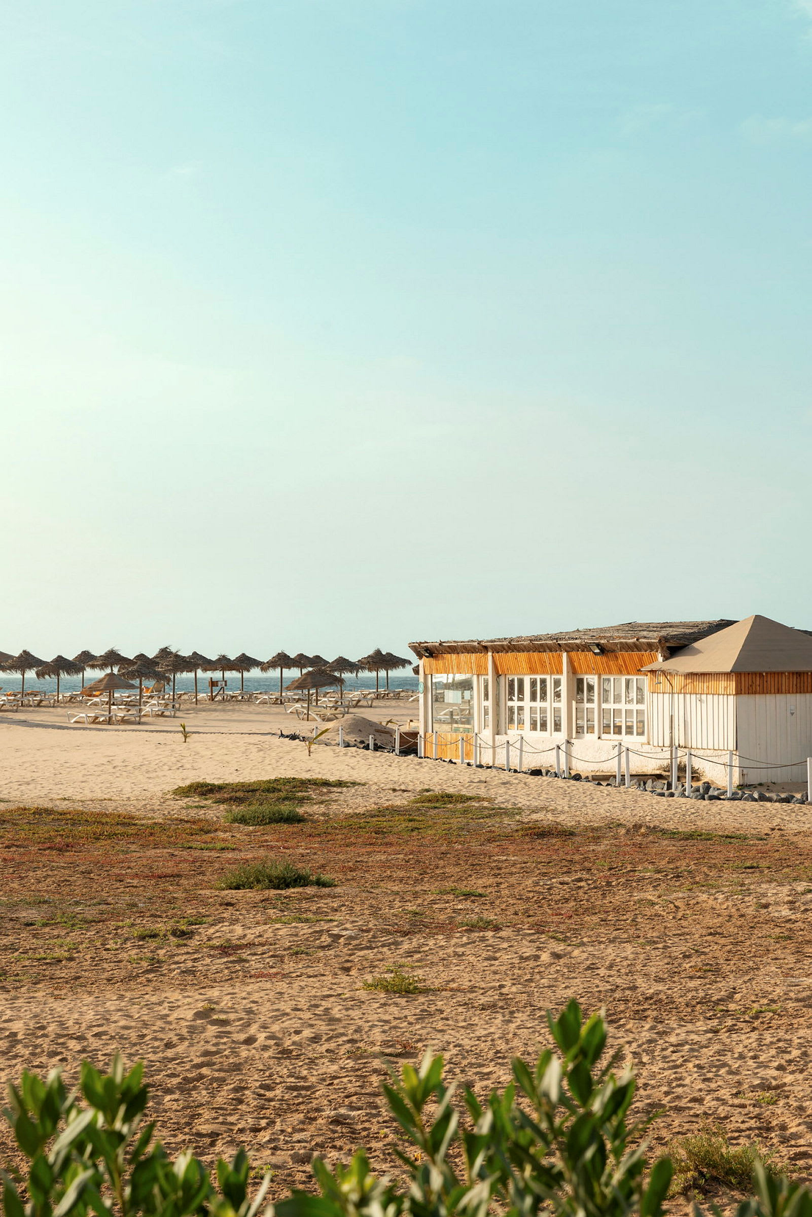 Strand med parasoller og en træbygning. (AI-genereret tekst)