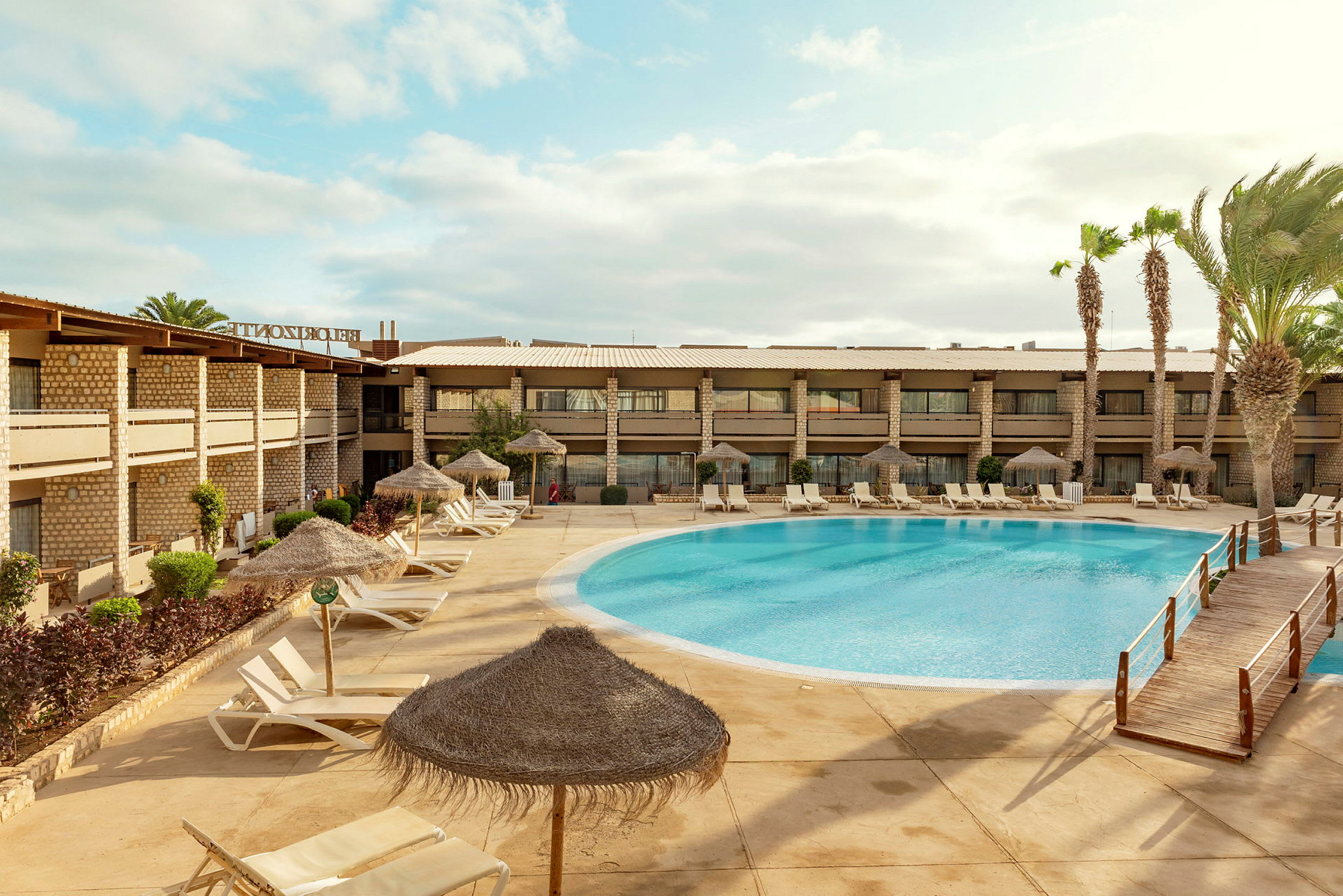 Hotelbygning ved en udendørs pool med liggestole og parasoller. (AI-genereret tekst)