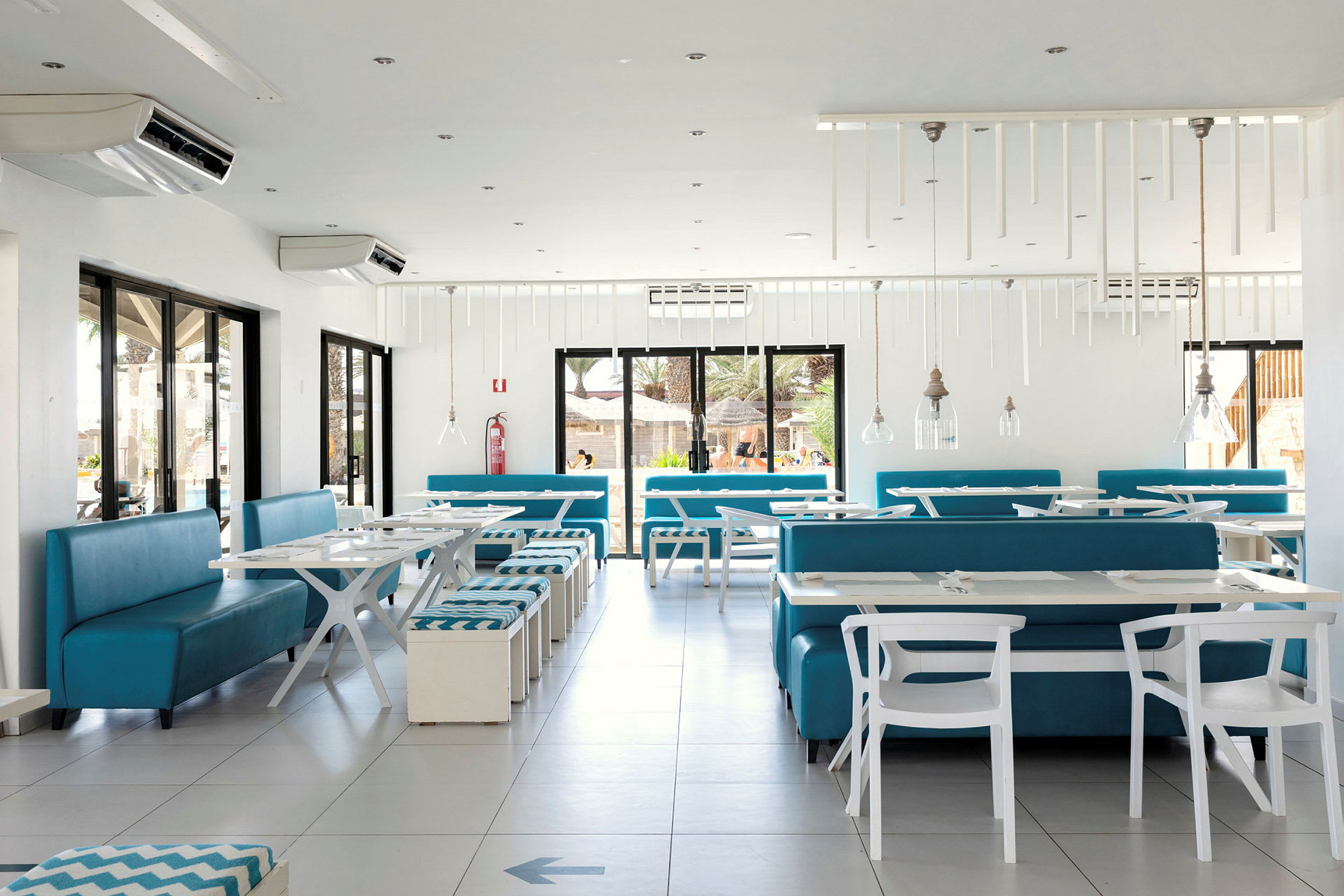 Lys og moderne restaurant med hvide borde og blå siddepladser. (AI-genereret tekst)