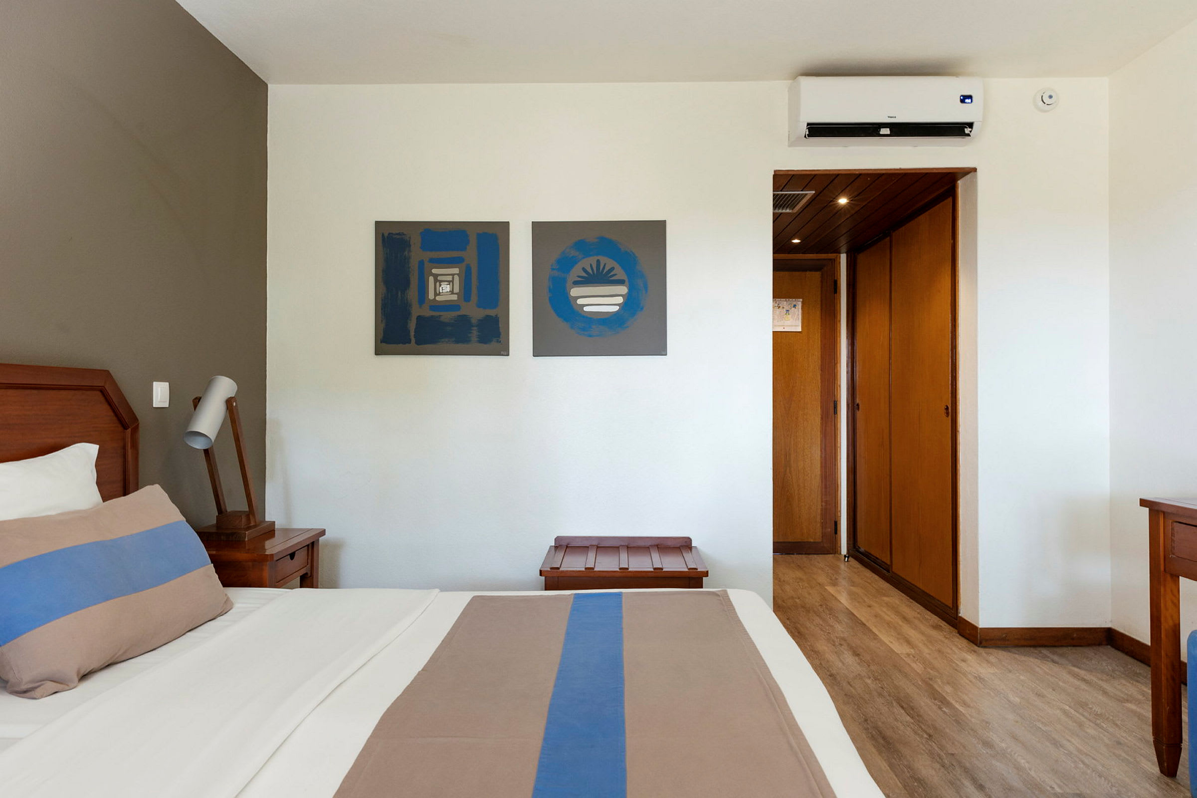 Hotelværelse med seng, natbord, kunst på væggene og en klimaanlægsenhed. (AI-genereret tekst)
