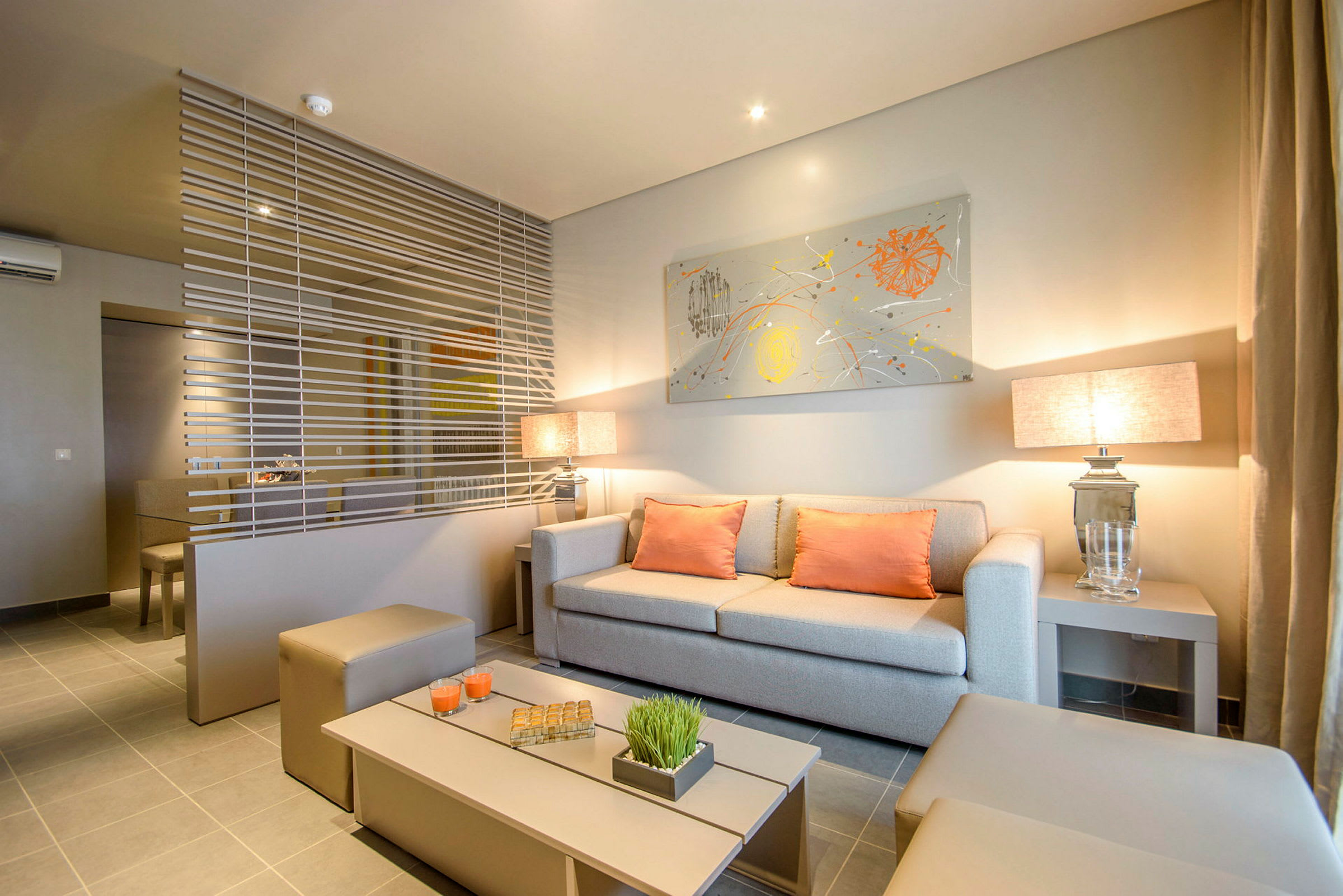 Stue med moderne indretning, beige sofa og orange puder, adskilt med dekorativt vandret net. (AI-genereret tekst)