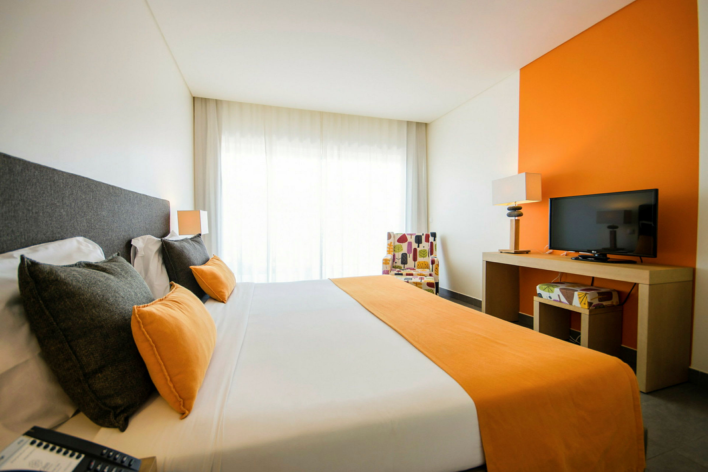 Billede af et hotelværelse med en dobbeltseng, orange detaljer og et tv på en bord. (AI-genereret tekst)