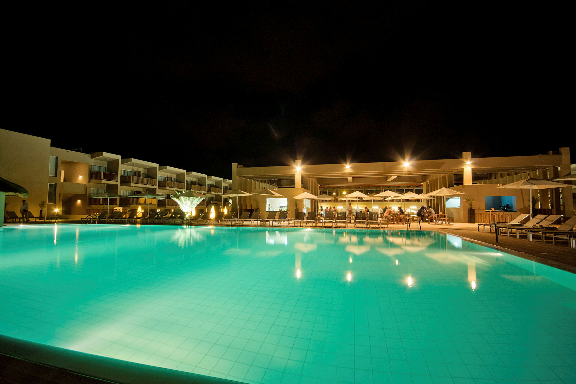 Hotellets pool og bygning oplyst om aftenen. (AI-genereret tekst)