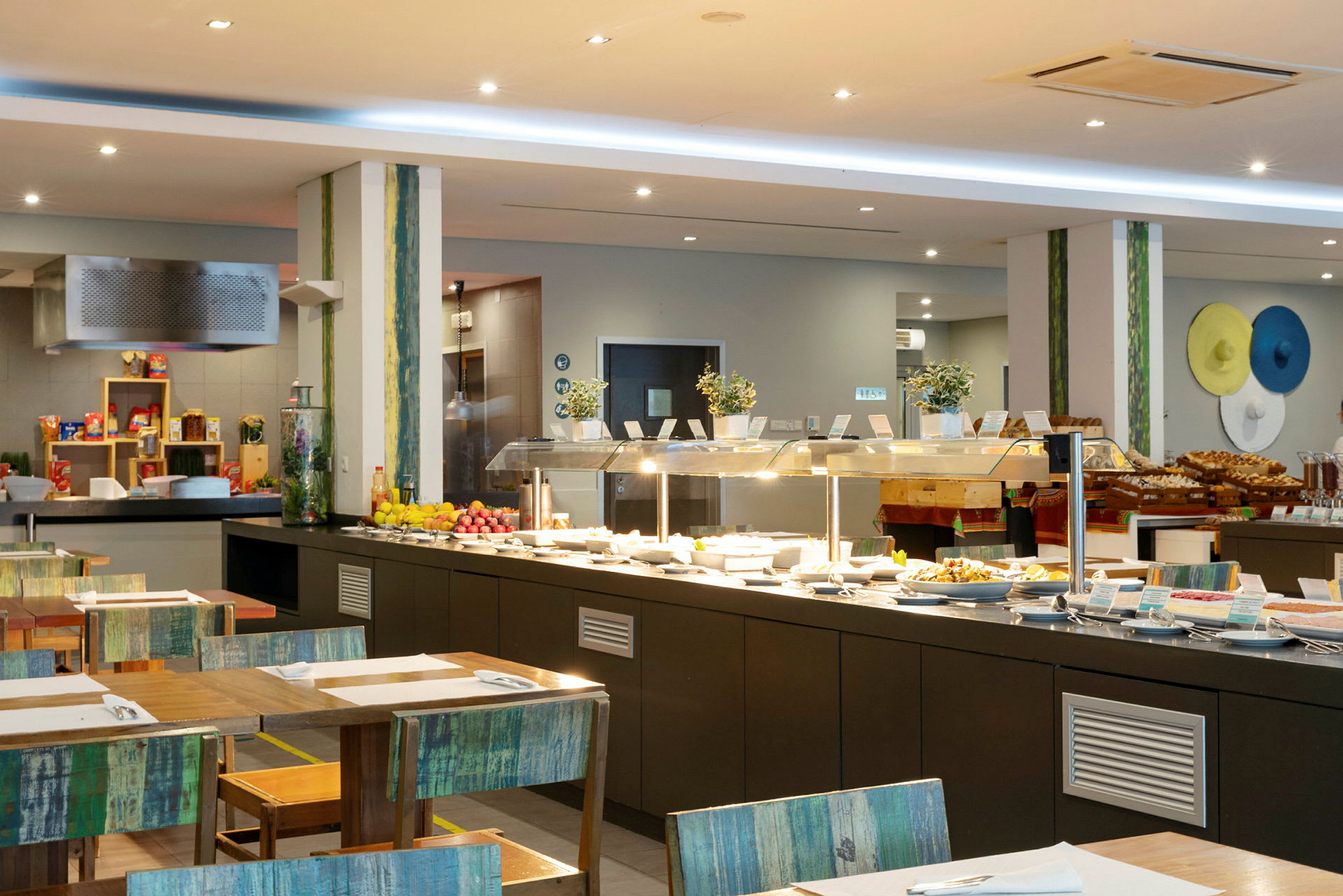 Interiør af en buffetrestaurant med serveringsborde fyldt med forskellige retter og frugter. (AI-genereret tekst)