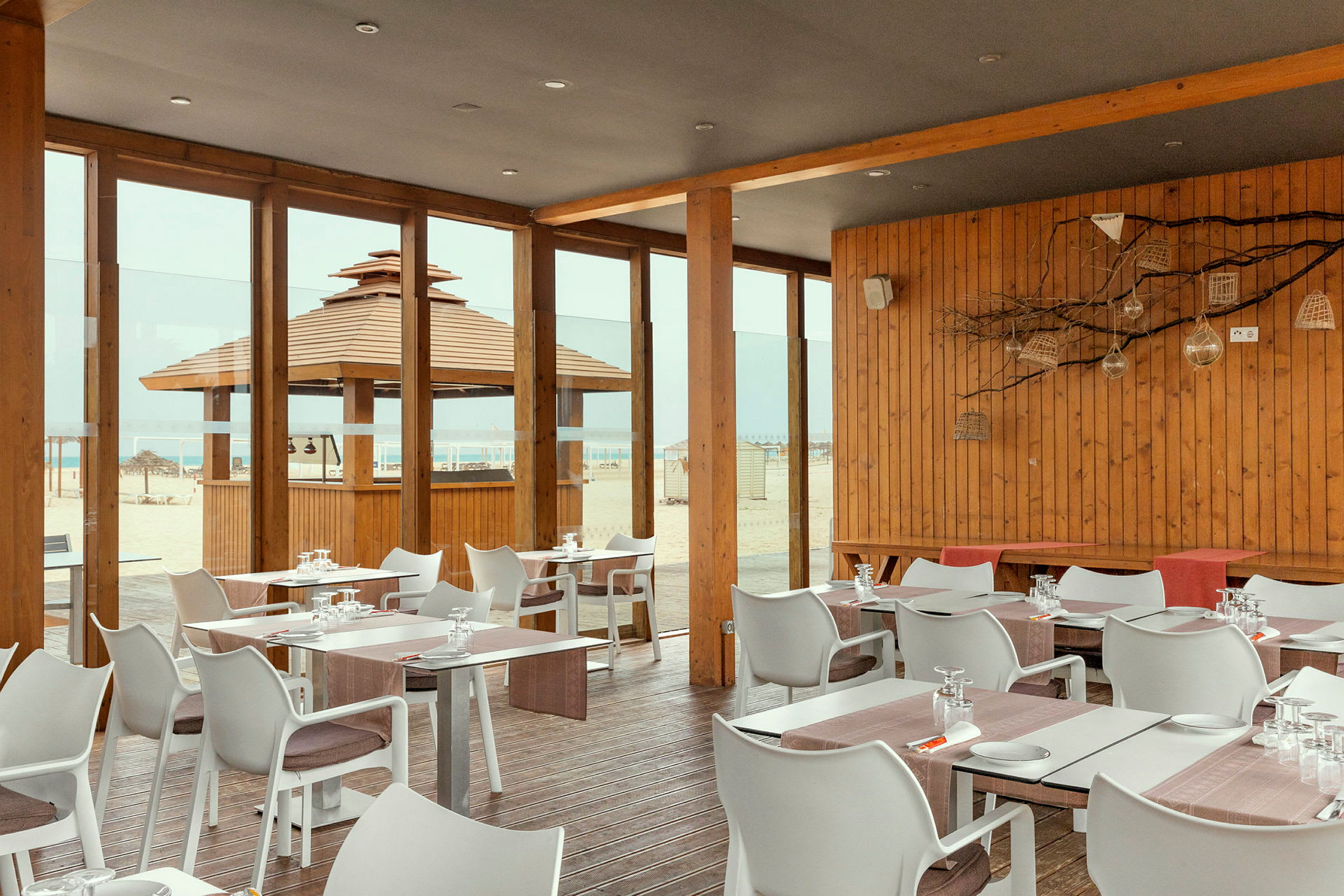 Restaurant med træpaneler og glasvægge med udsigt til stranden. (AI-genereret tekst)