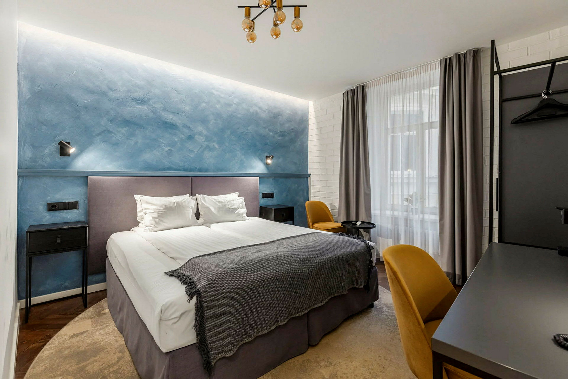 Et hotelværelse med en dobbeltseng, blå væg og gule stole. (AI-genereret tekst)