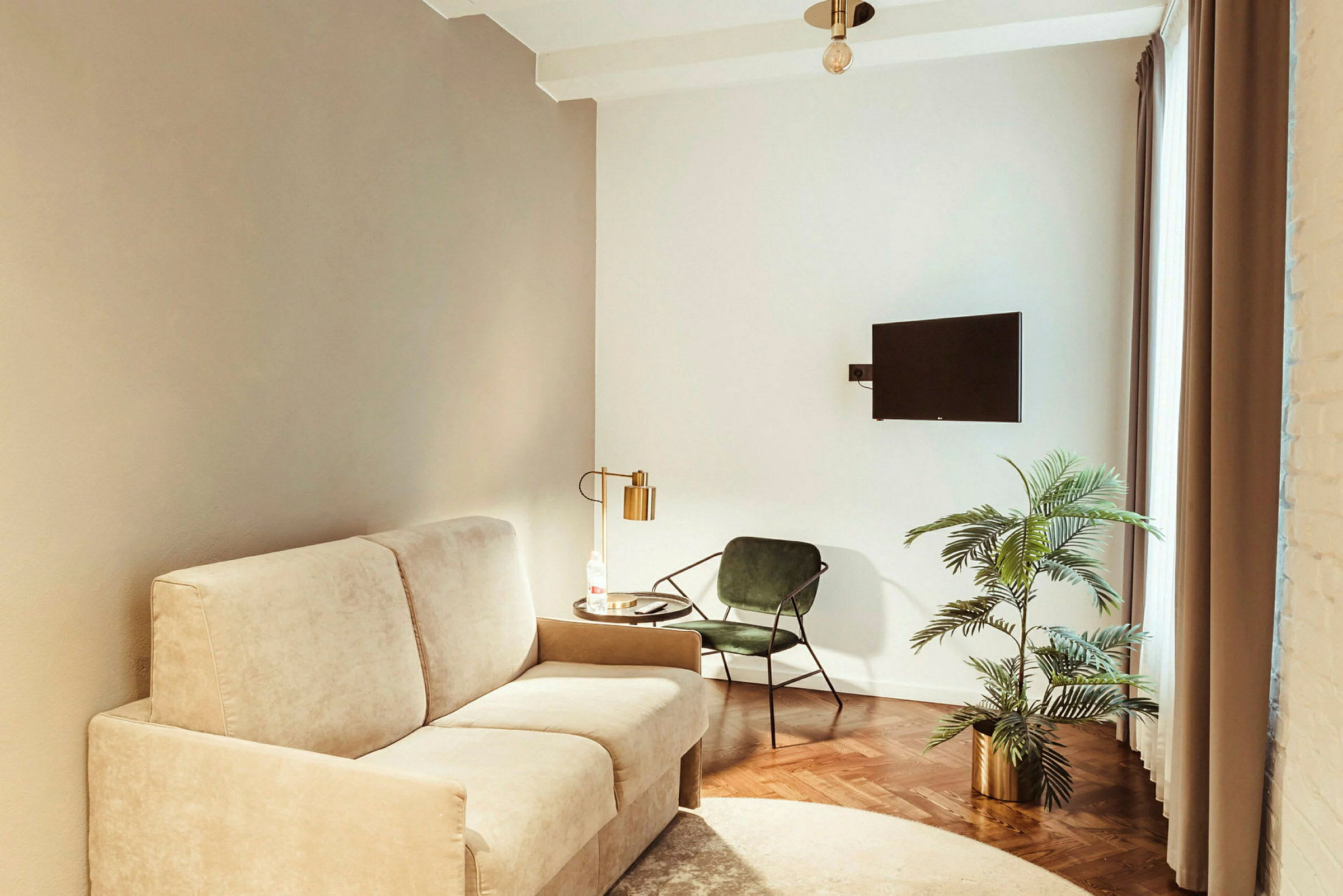 En stue med beige sofa, grøn stol, bord med lampe, plante i urtepotte og vægmonteret fjernsyn. (AI-genereret tekst)