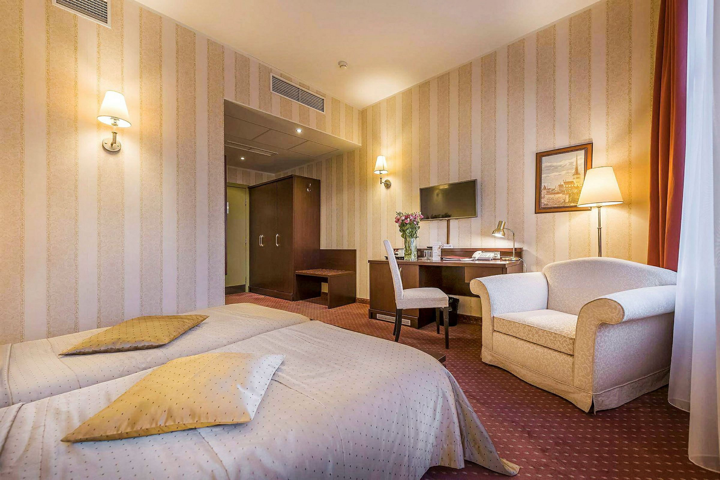 Hotelværelse med to enkeltsenge, skrivebord med stol, tv på væggen og en lænestol. (AI-genereret tekst)