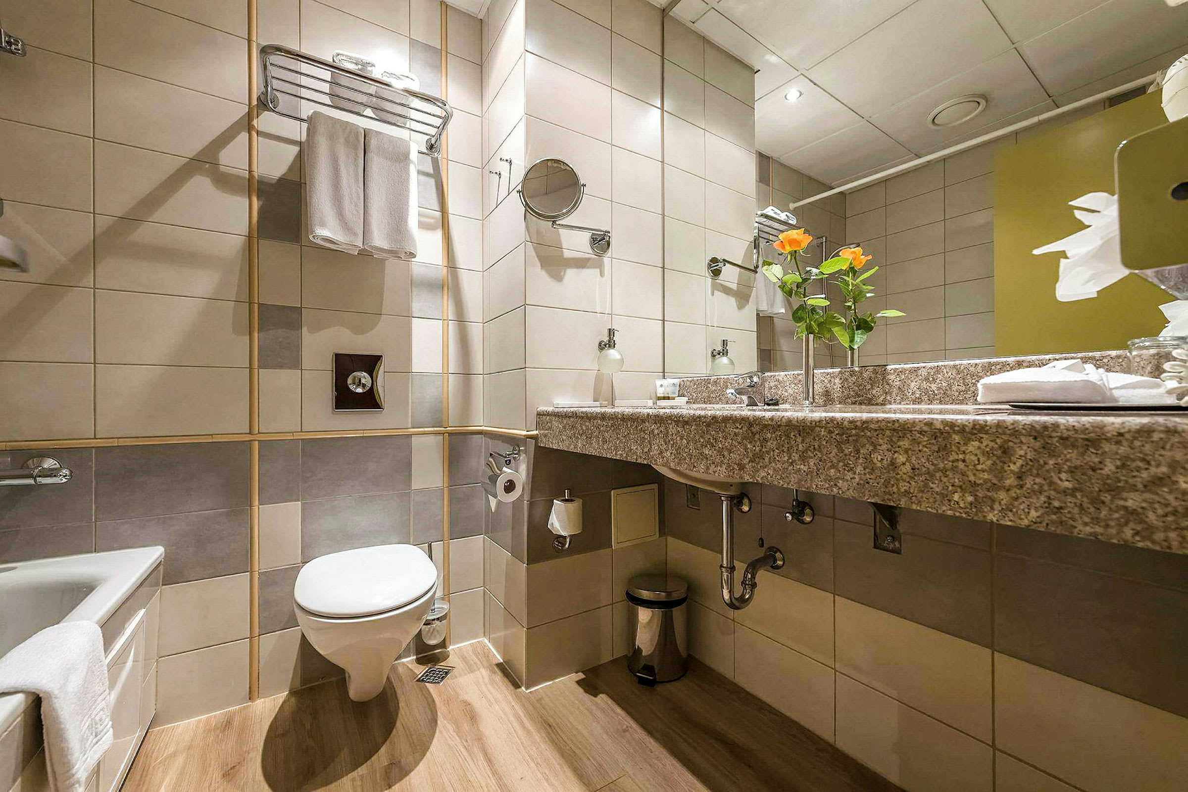 Badeværelse med toilet, vask og bruser/badekar samt dekorationer som blomster og håndklæder. (AI-genereret tekst)