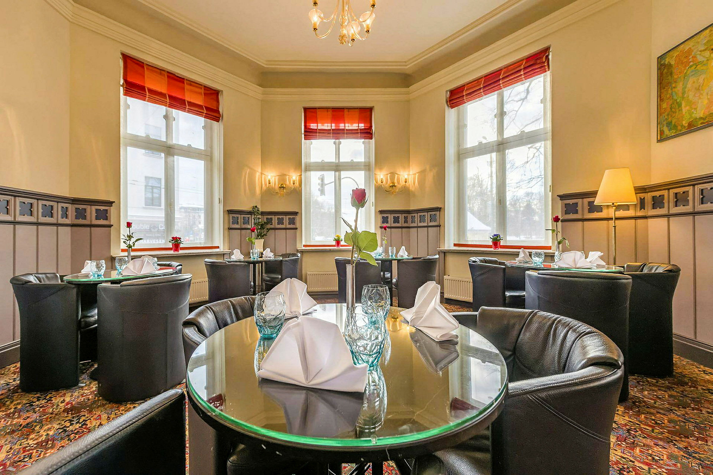 Interiør af en restaurant med dækkede, runde borde og store vinduer. (AI-genereret tekst)