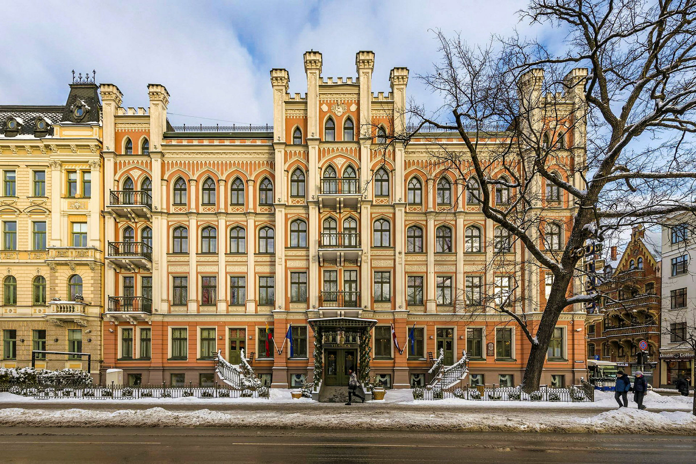 Facaden af en statelig bygning med gotisk arkitektur og mange vinduer, set om vinteren med sne på jorden. (AI-genereret tekst)