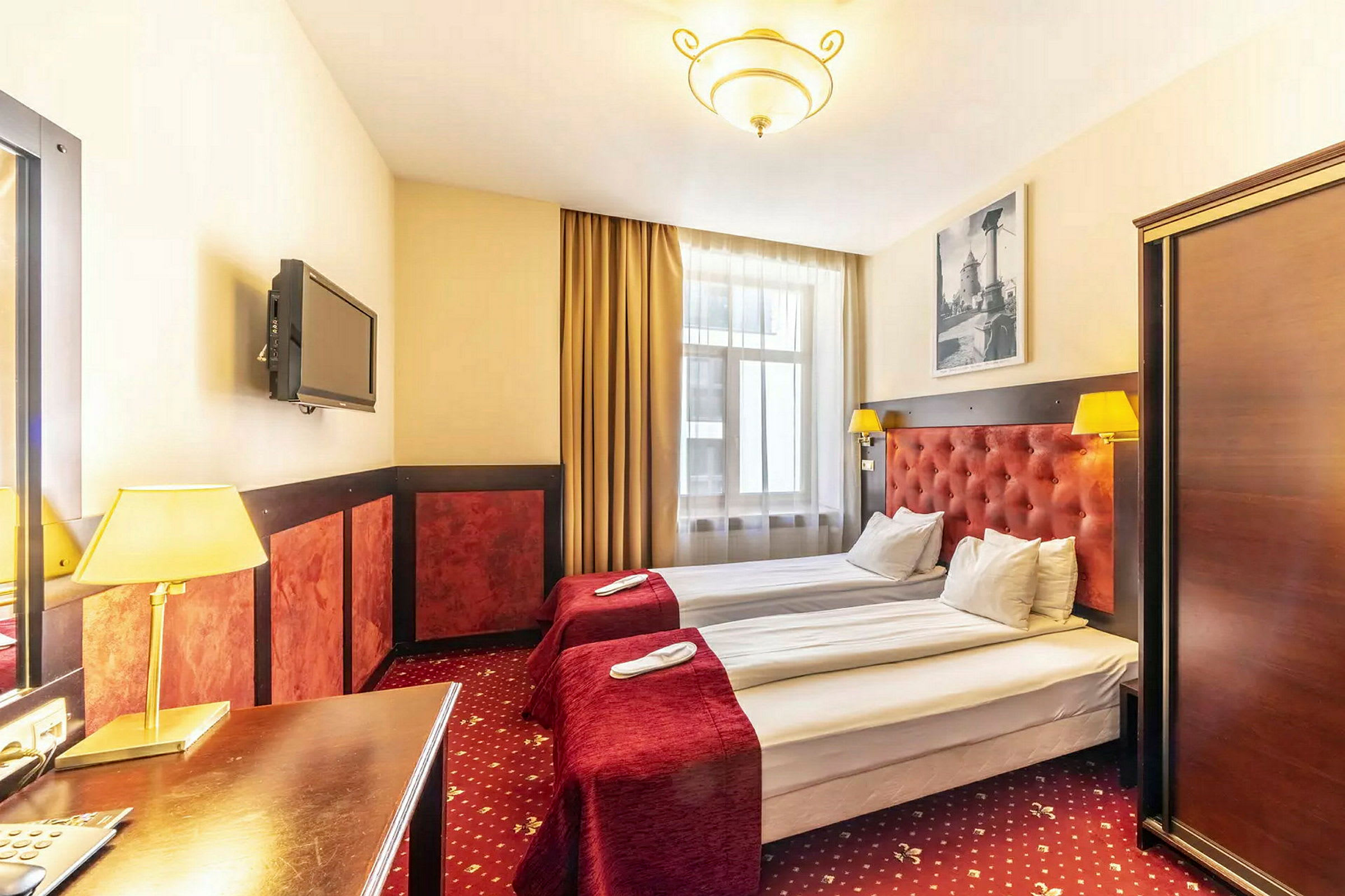 Hotelværelse med to enkeltsenge, røde sengetæpper og lamper. (AI-genereret tekst)
