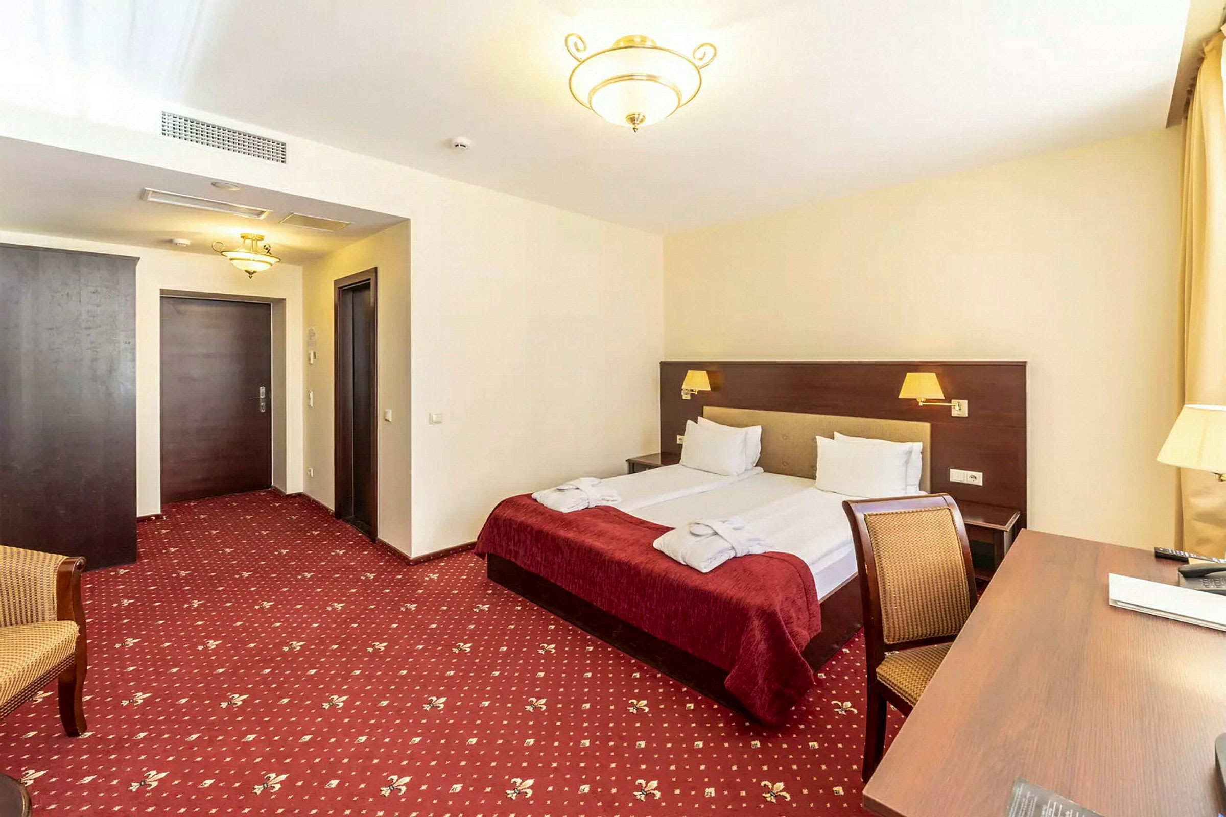 Hotelværelse med dobbeltseng, skrivebord og stol. (AI-genereret tekst)
