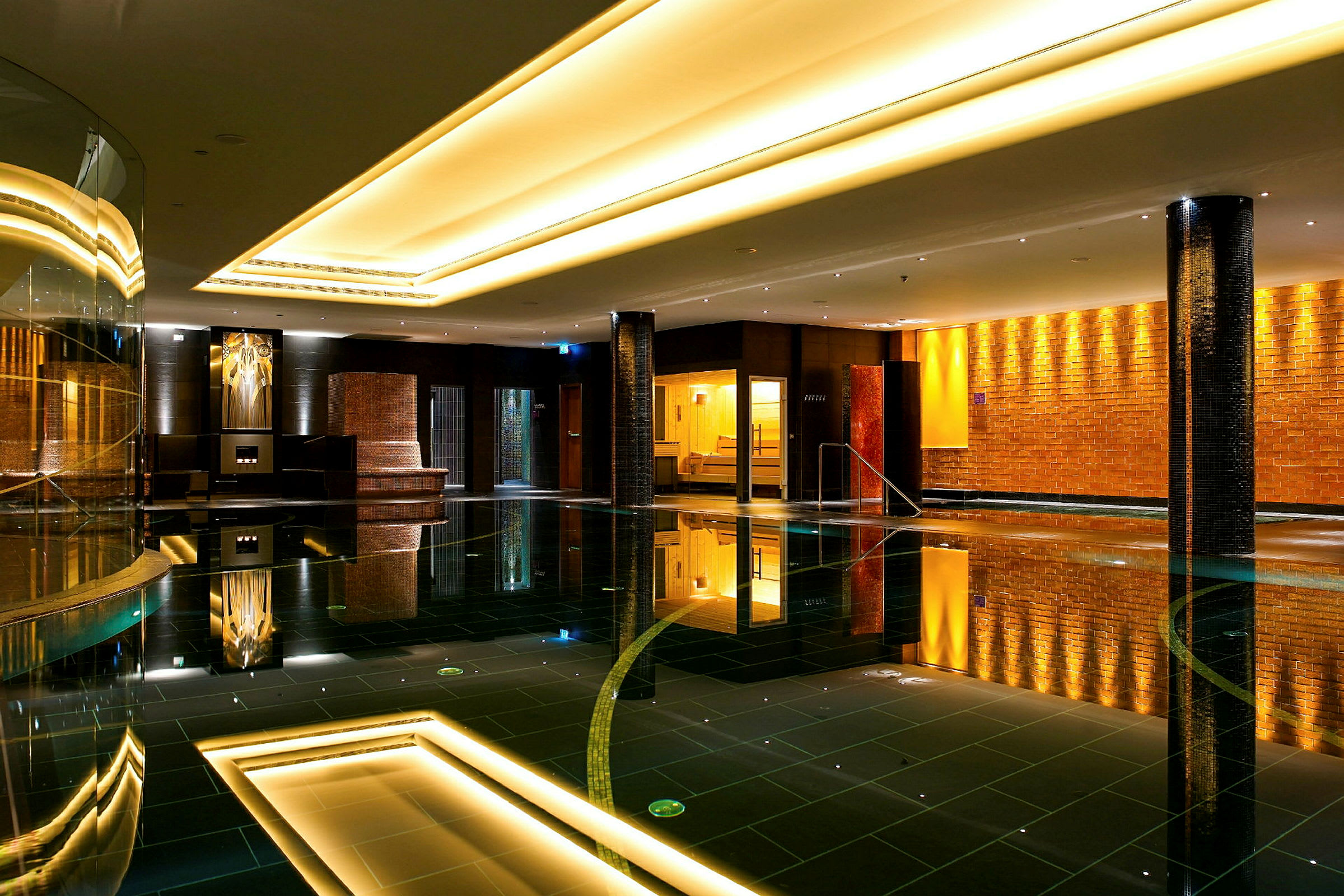 Et elegant badeområde med en stor indendørs pool omgivet af moderne interiørdetaljer og varm belysning. (AI-genereret tekst)