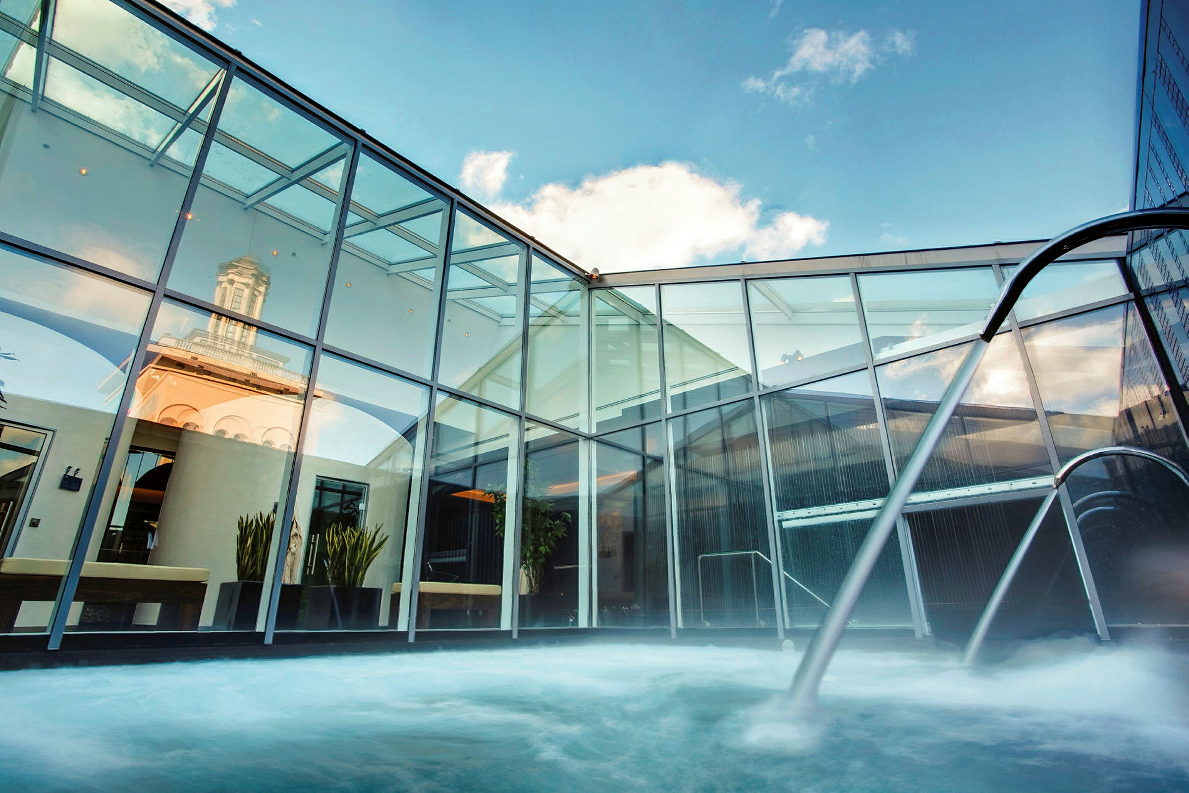 Et moderne spa med en udendørs pool omgivet af glasvægge og himmelen i baggrunden. (AI-genereret tekst)