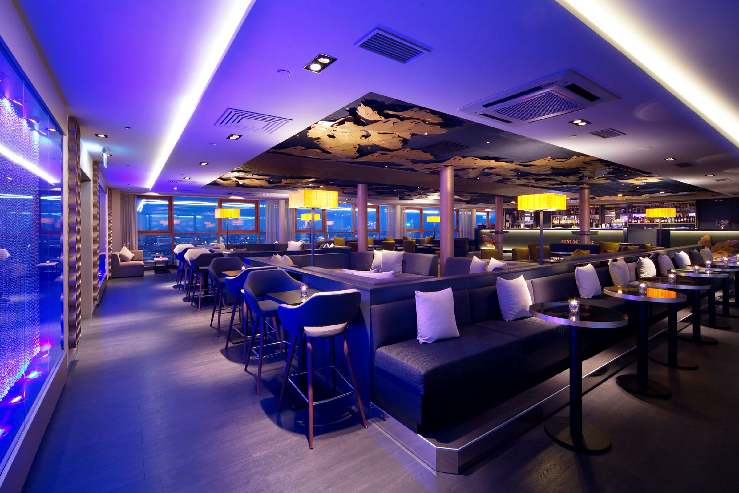 Et elegant lounge- og barområde med moderne møbler, stemningsfuld belysning og store panoramavinduer. (AI-genereret tekst)