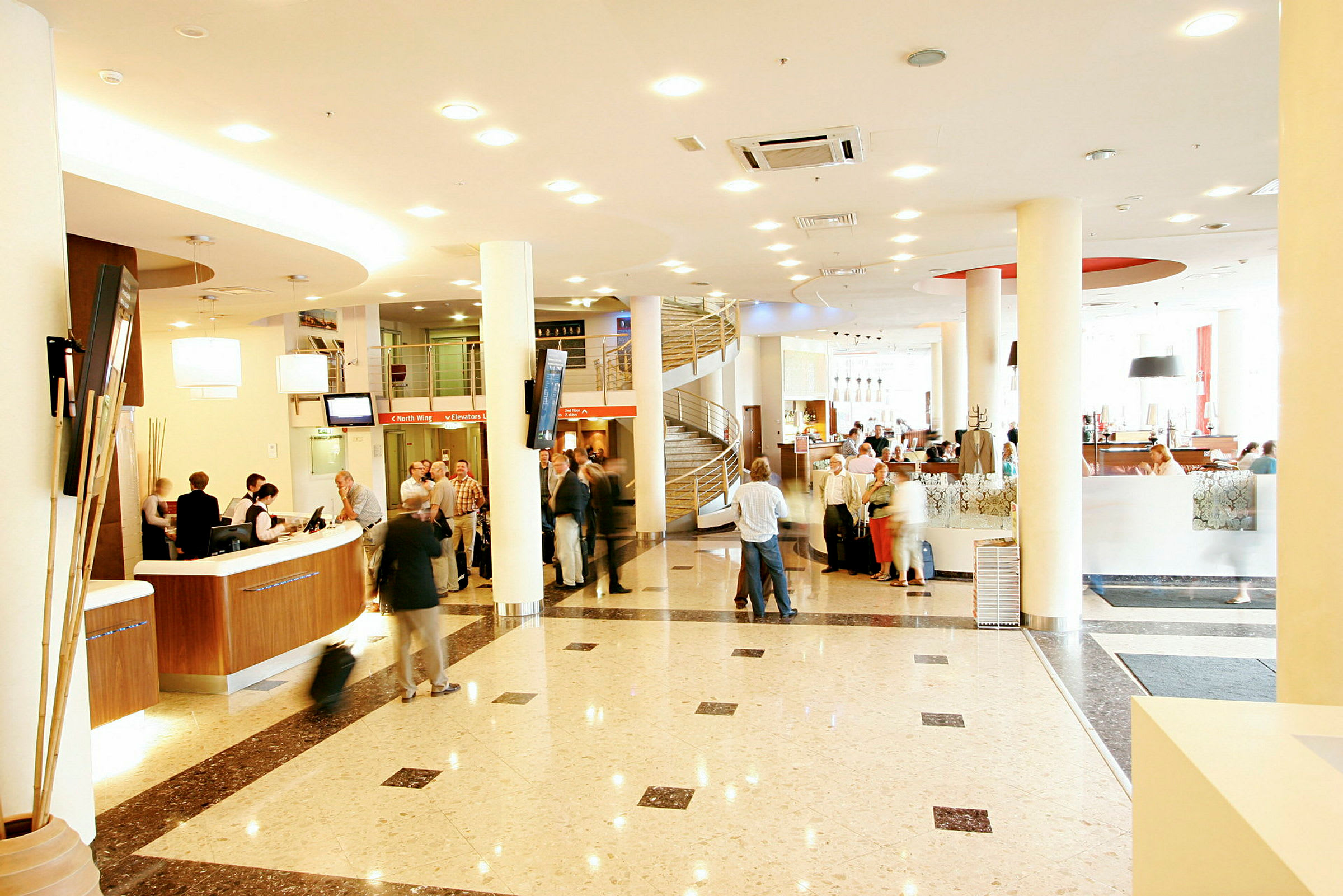 En hotellobby med reception, personer der venter, lys indretning og marmorgulv. (AI-genereret tekst)
