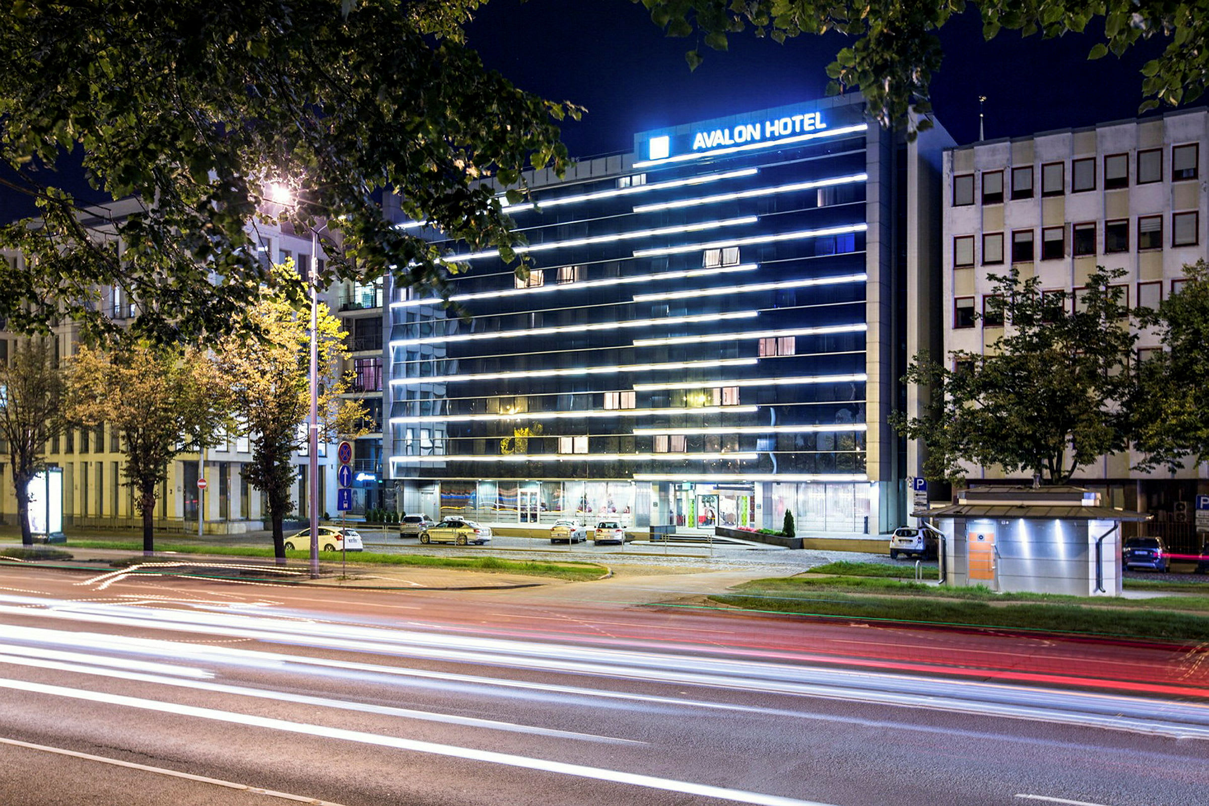 Et hotel ved en gade med lyse facader og belysning om natten. (AI-genereret tekst)