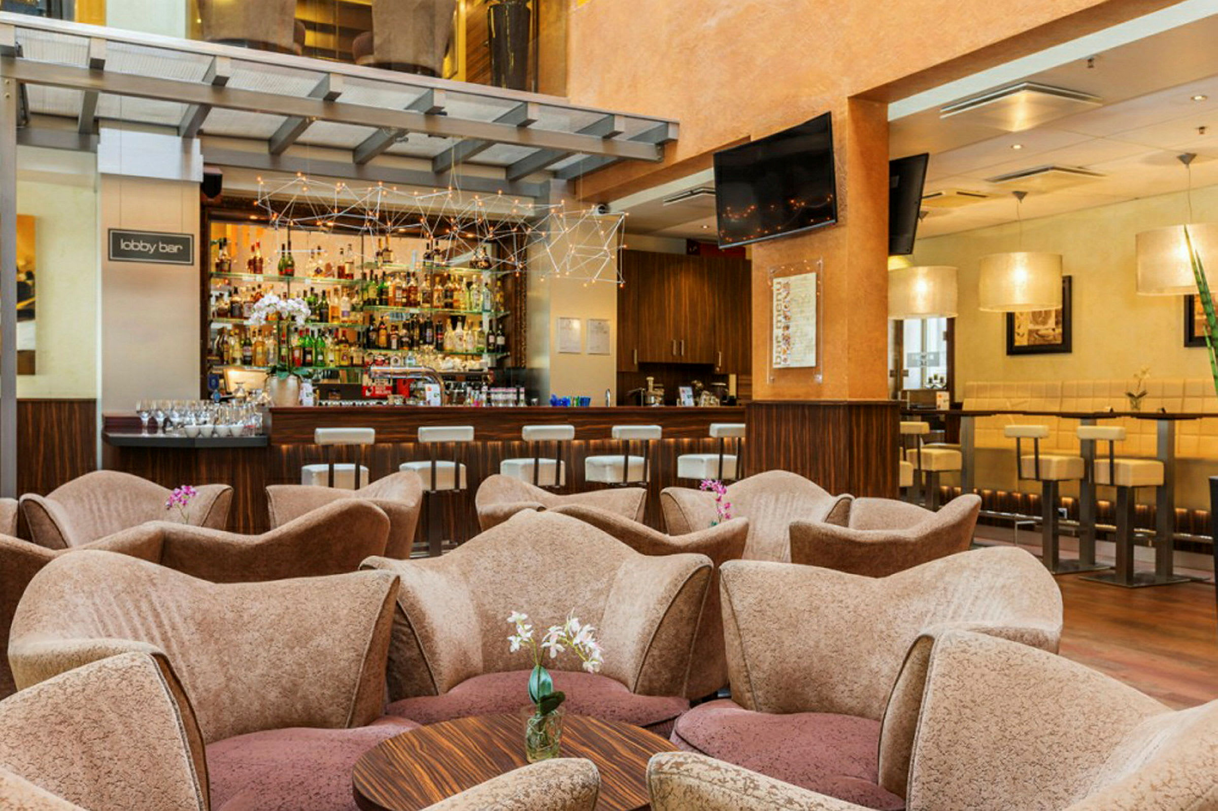 Billede af en lobbybar med sofaer og et bord i forgrunden samt en bar med flasker og siddepladser i baggrunden. (AI-genereret tekst)