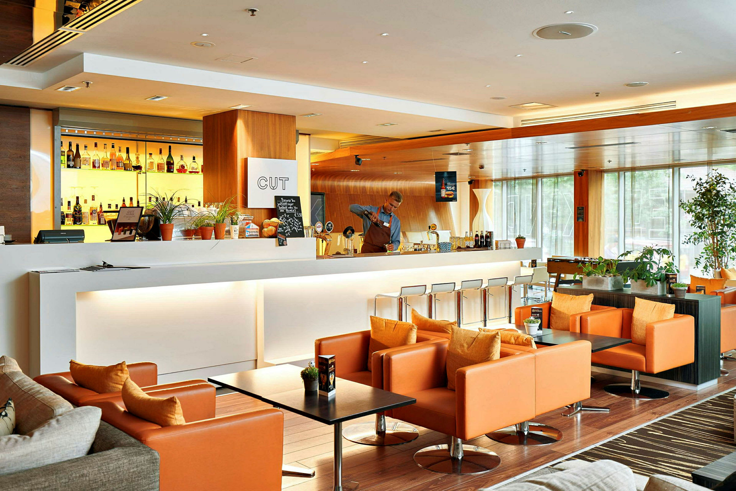 En moderne og elegant lounge med en hvid bardisk, baggrundsbelyste spiritusflasker og komfortable orange lænestole. (AI-genereret tekst)