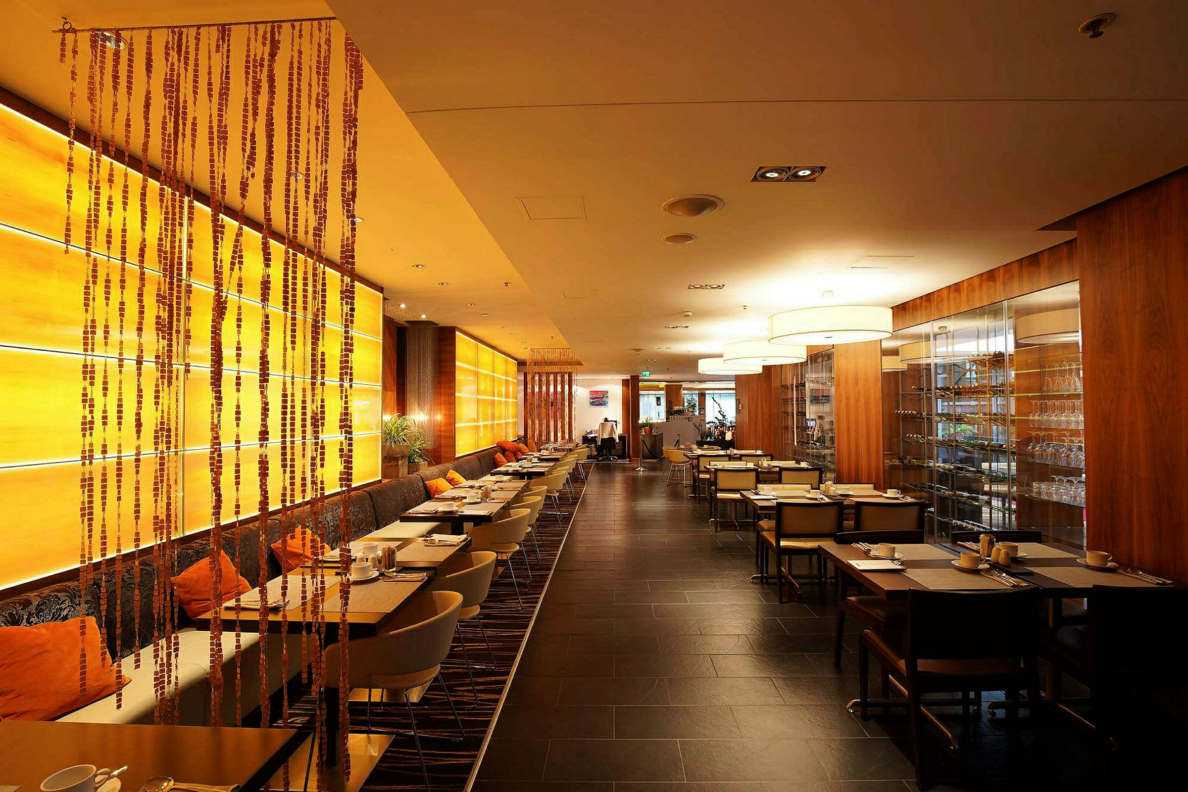 Billede af en restaurant med moderne møbler, varme farver og række af dækte borde. En hylde med glas er synlig til højre. (AI-genereret tekst)