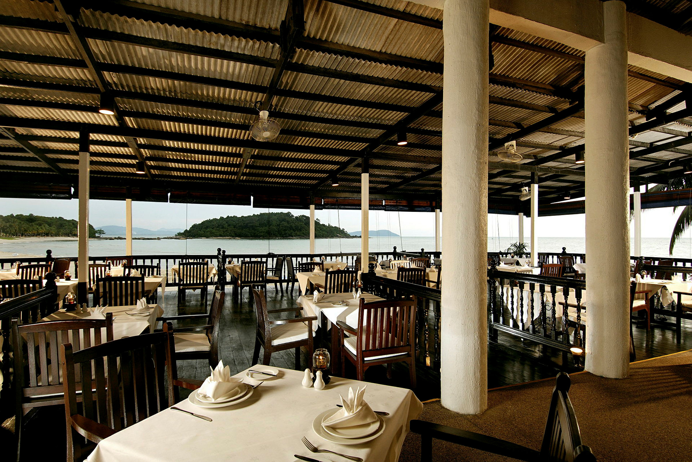 En restaurant med træborde og stole med udsigt til havet gennem store vinduer. (AI-genereret tekst)