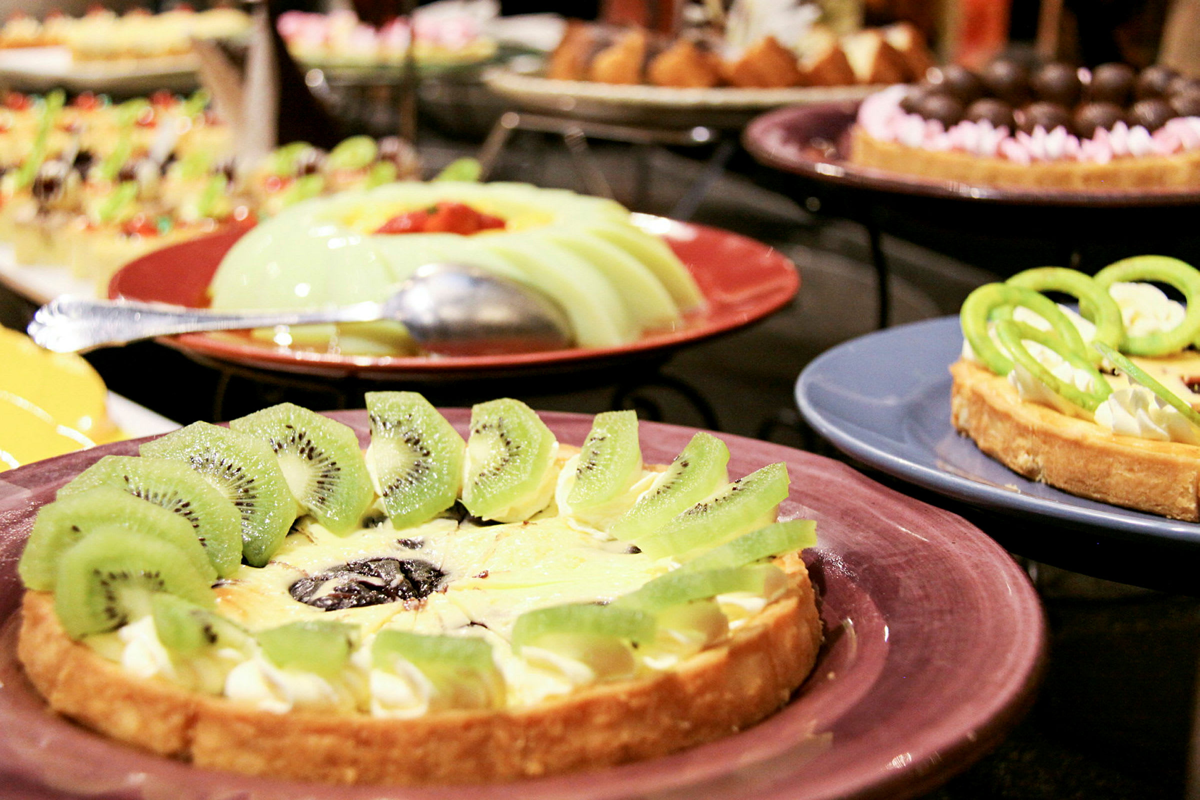 Forskellige desserter, herunder en tærte dekoreret med kiwi på en tallerken. (AI-genereret tekst)