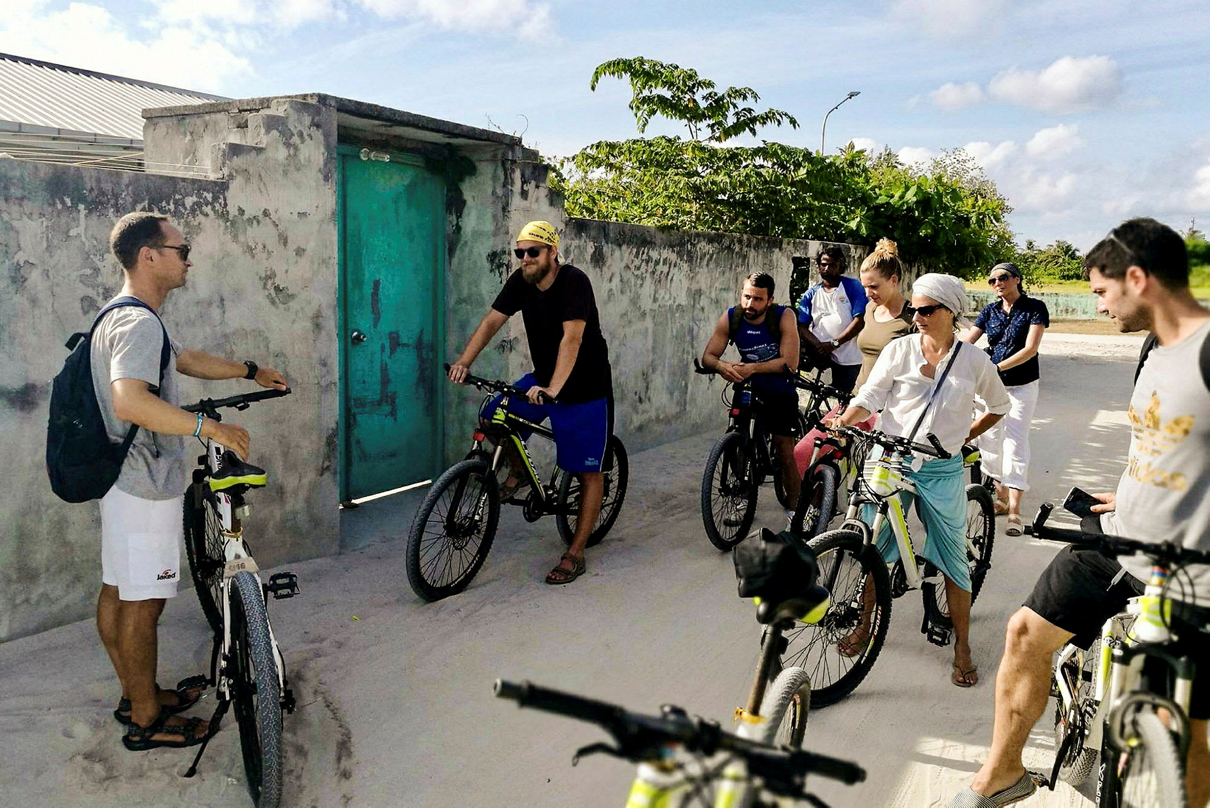 En gruppe cyklister står ved en betonvæg med en grøn dør omgivet af grønne omgivelser. (AI-genereret tekst)