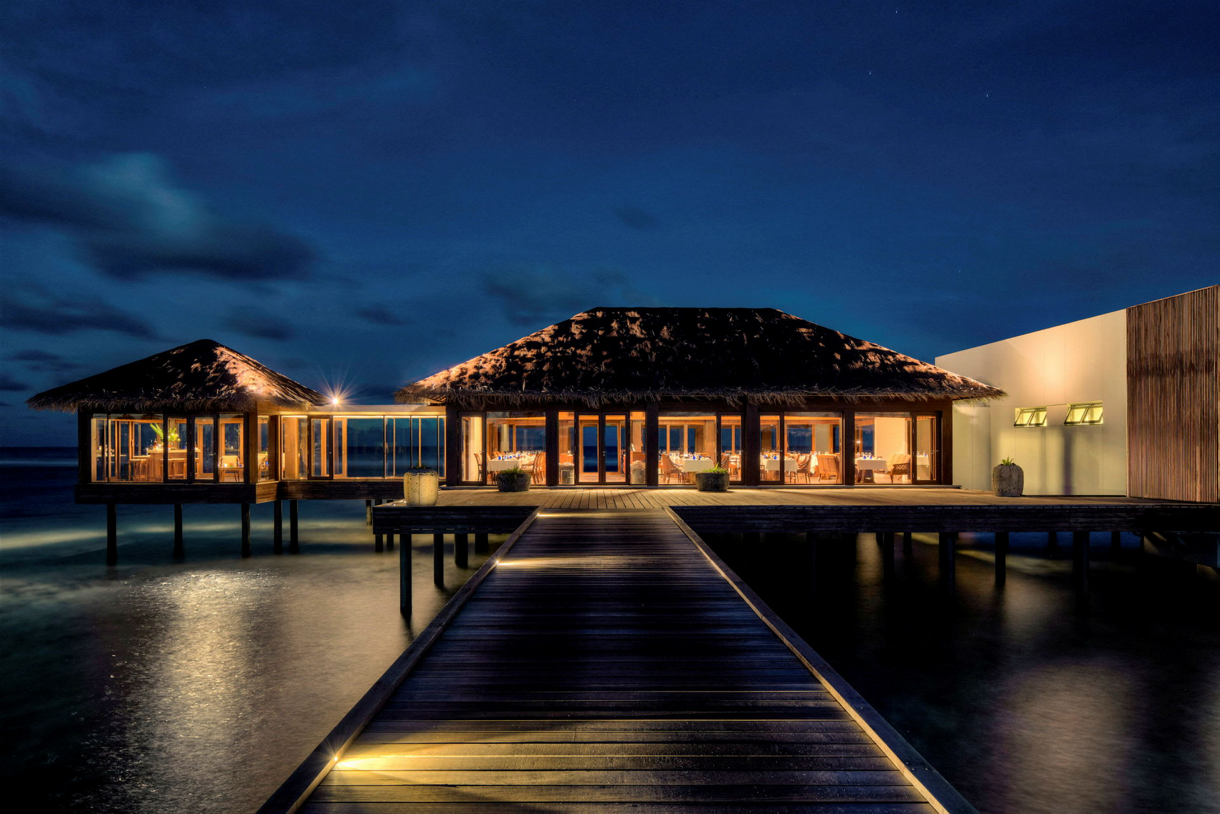 Billede af en oplyst strandvilla på pæle over havet, fotograferet om natten. (AI-genereret tekst)
