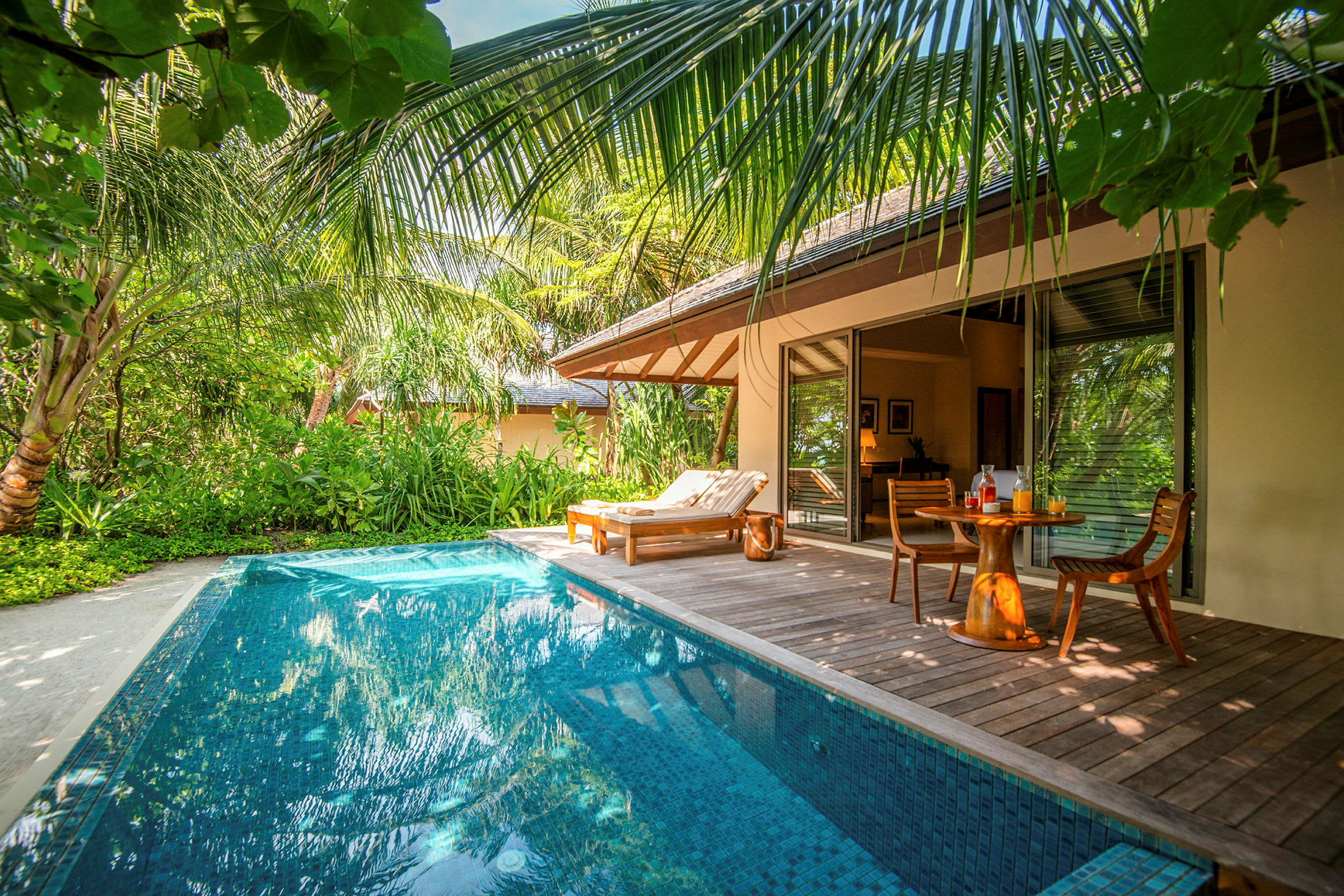 En privat pool ved en tropisk villa med en solseng og et bord med stole. (AI-genereret tekst)
