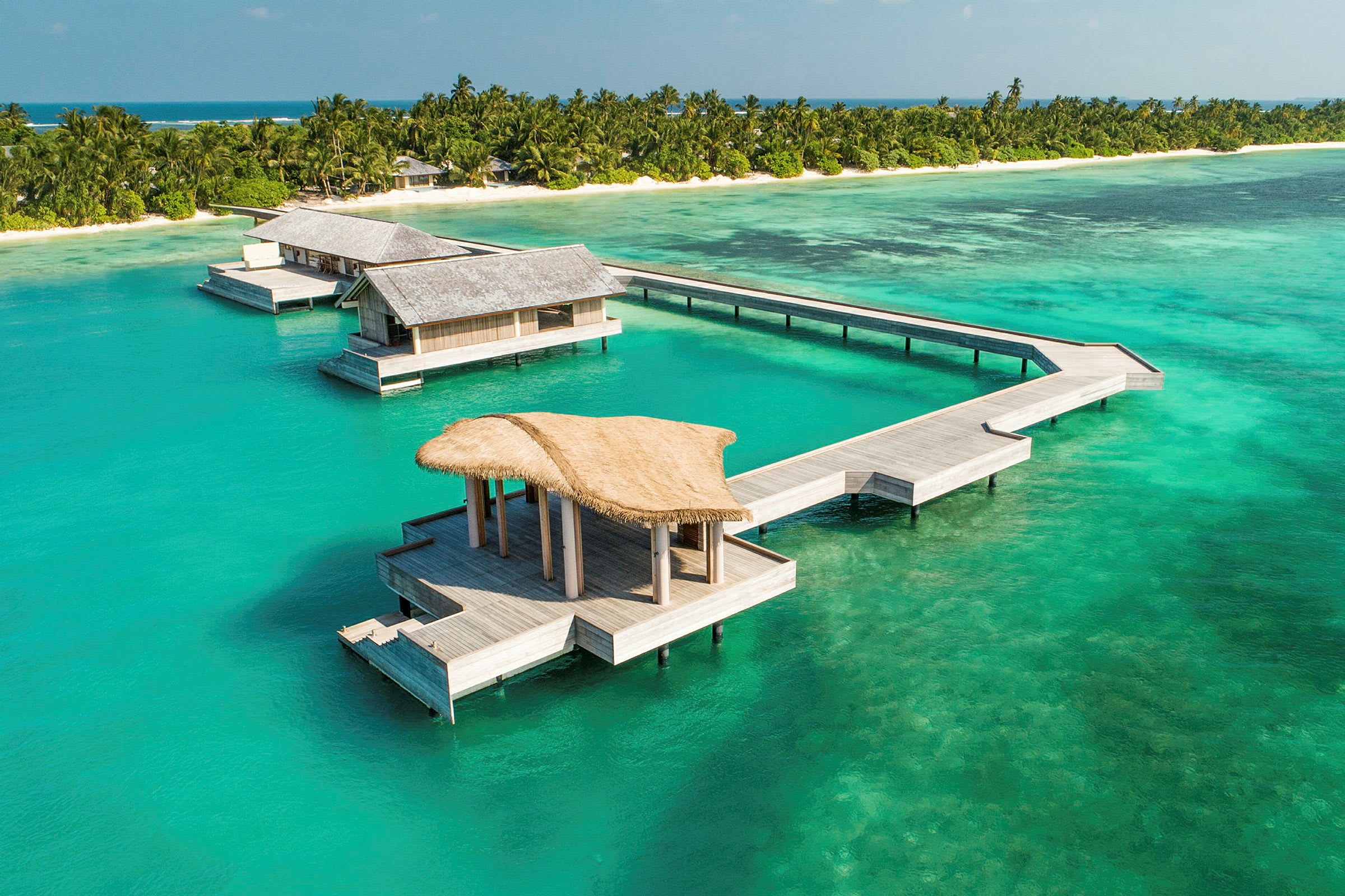 Overvandsbungalower ved en tropisk strand med turkis hav. (AI-genereret tekst)