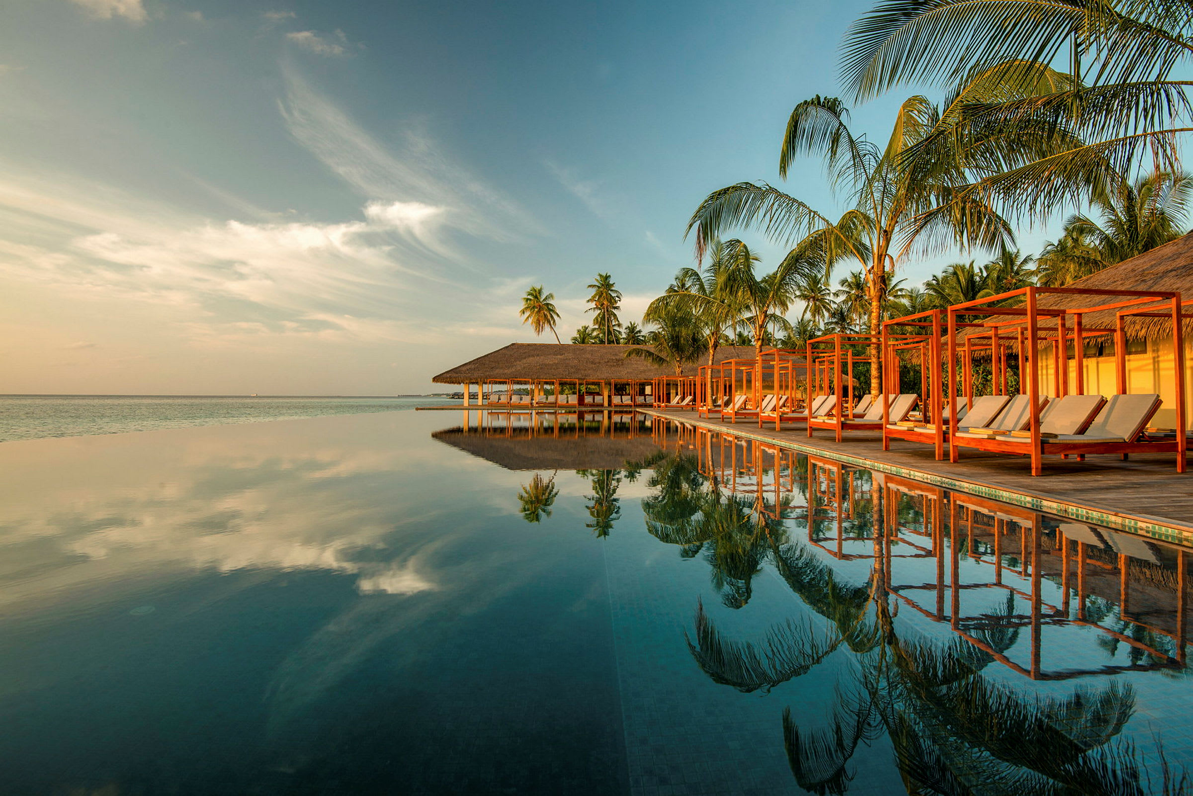 En infinitypool ved en tropisk resort med palmer og himmel, der spejles i vandet. (AI-genereret tekst)