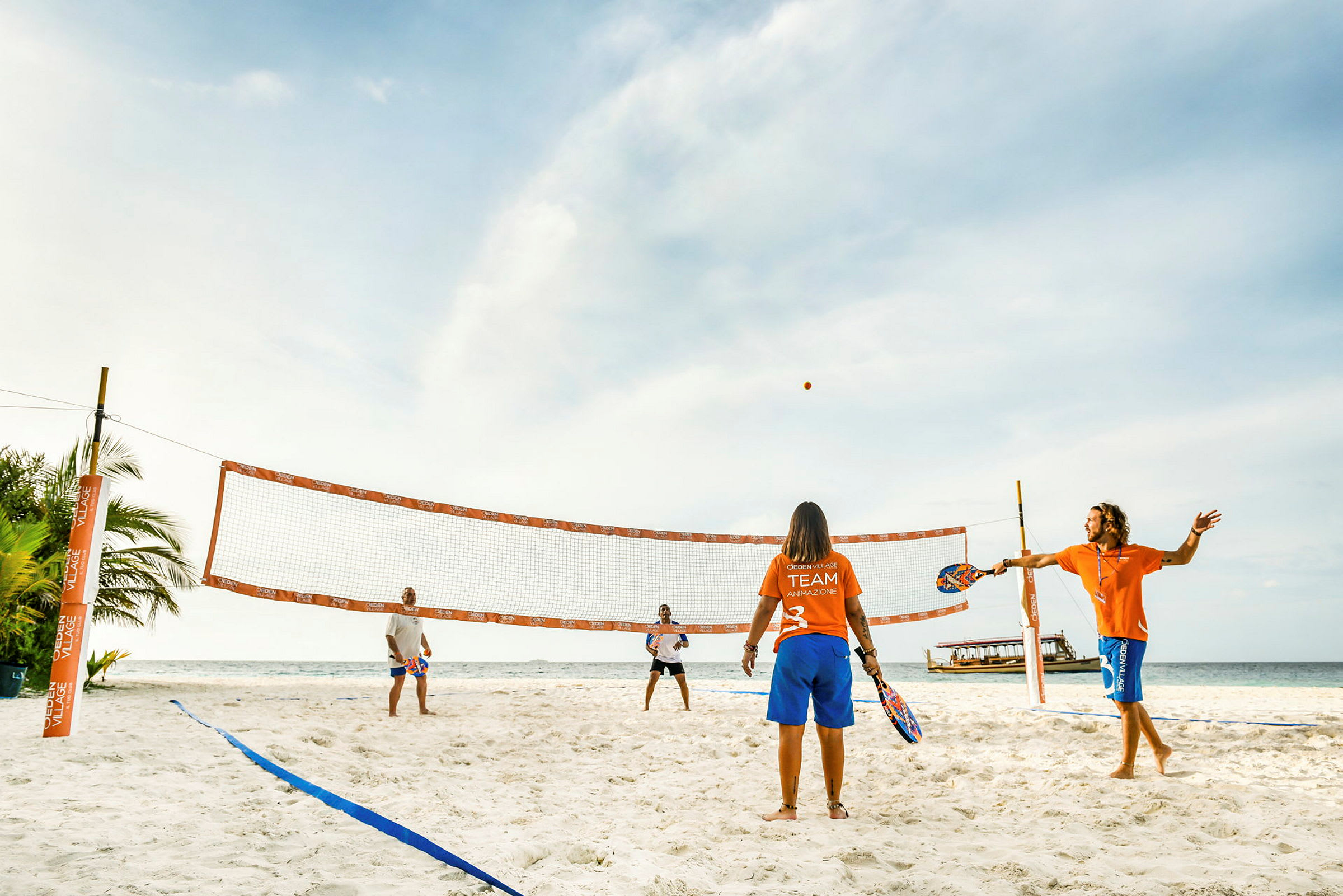 Fire personer spiller strandtennis på en solrig sandstrand. (AI-genereret tekst)