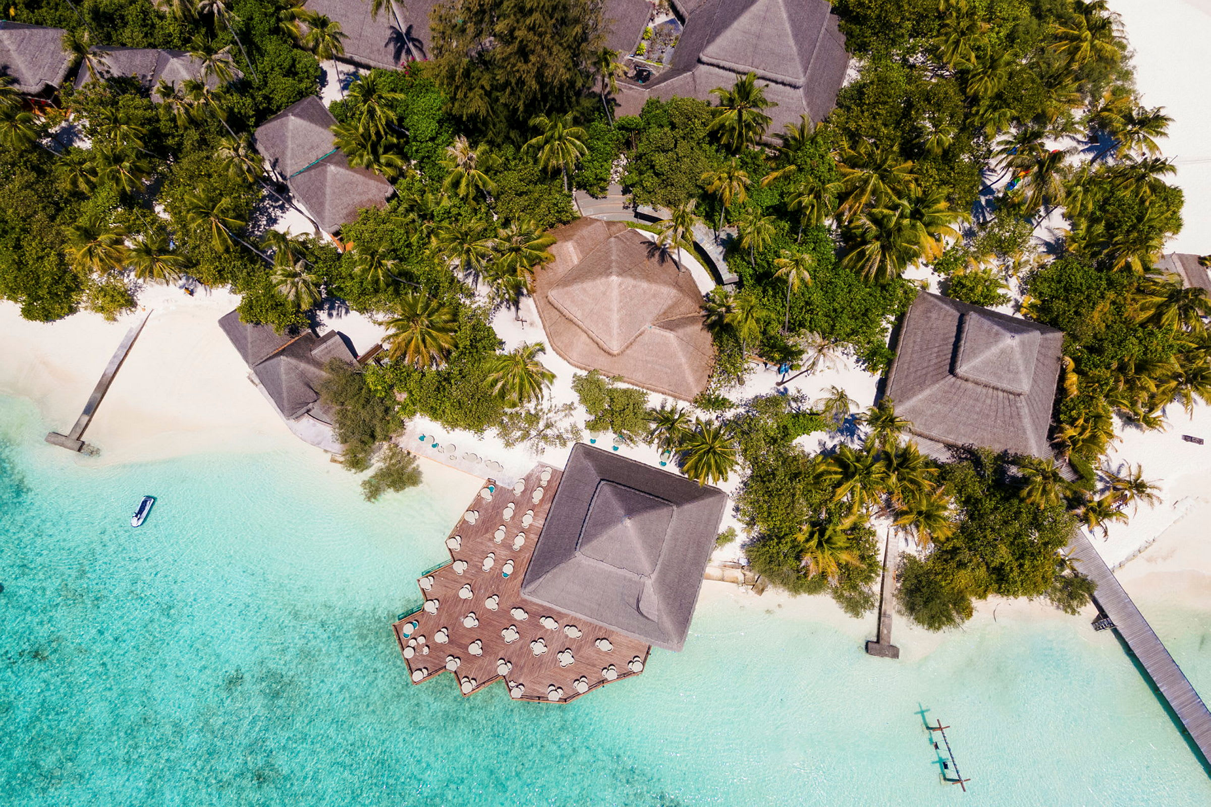 Luftfoto af tropisk resort med bungalower omgivet af frodig vegetation og klart blåt vand. (AI-genereret tekst)