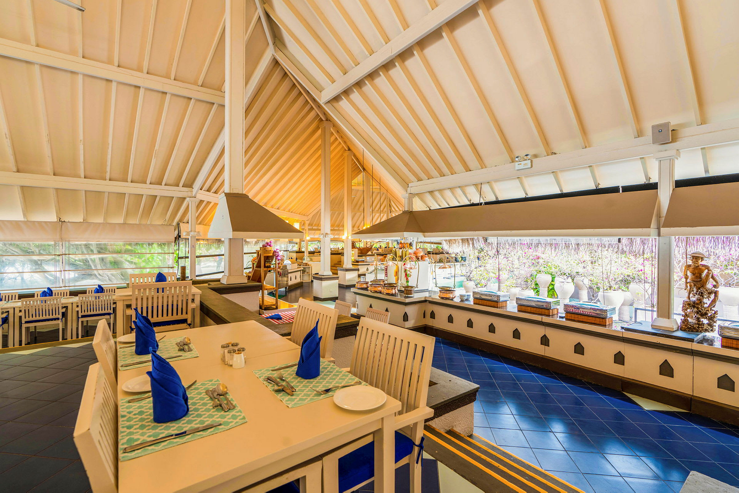 Interiør af en restaurant med dækkede borde, blå servietter og en buffet i baggrunden. (AI-genereret tekst)