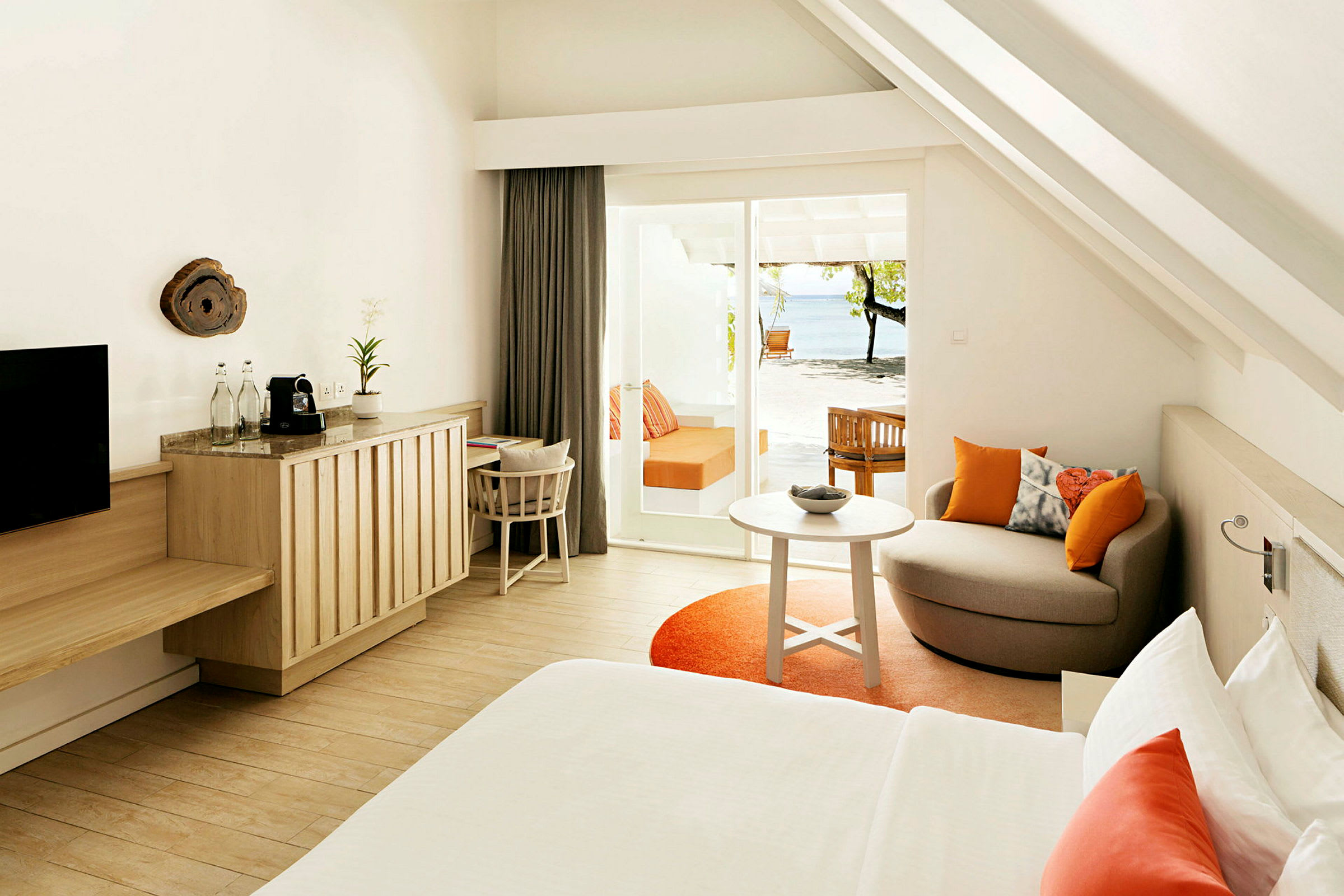 Et moderne hotelværelse med lyse trædetaljer, orange accentfarver og en terrasse med udsigt over stranden. (AI-genereret tekst)