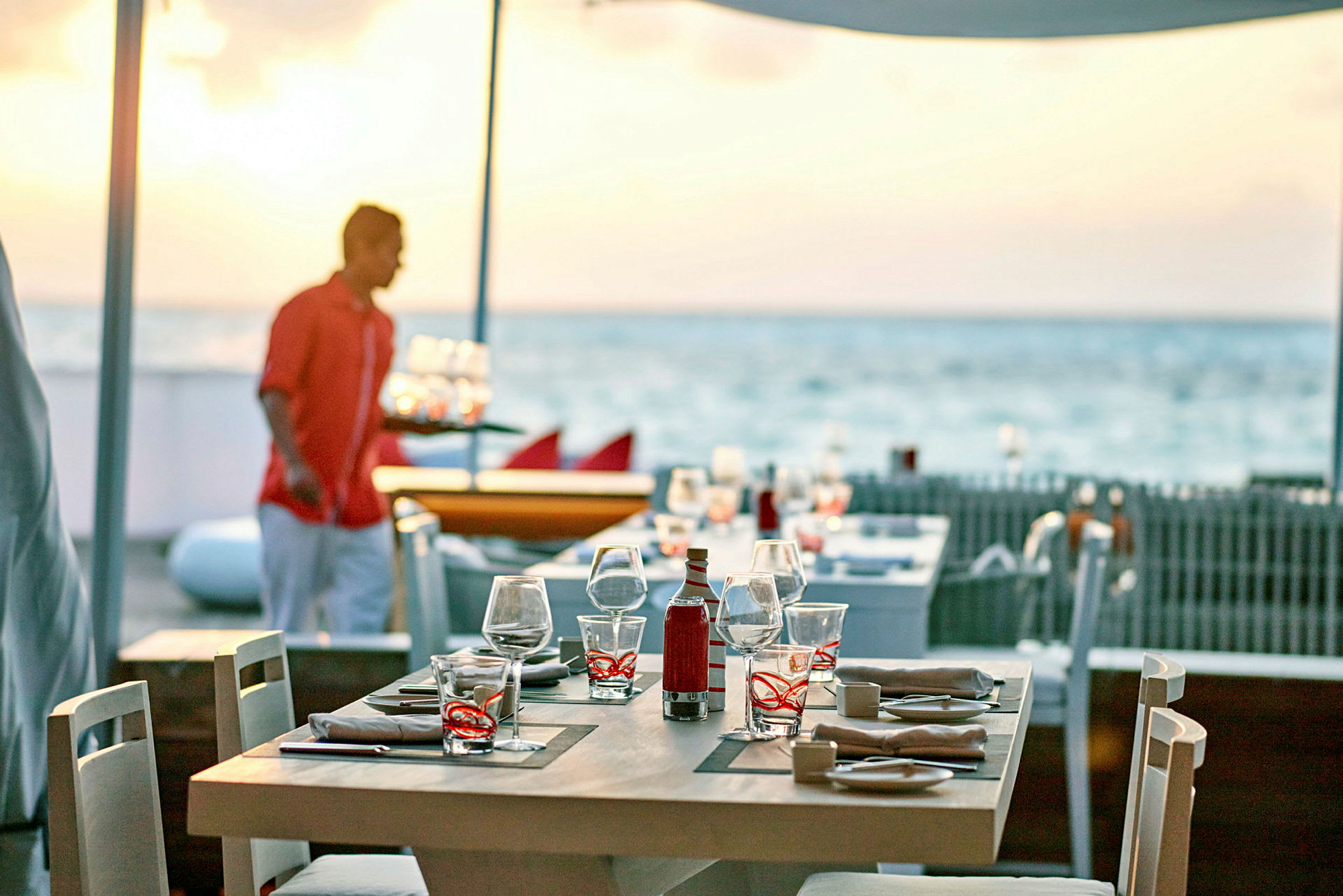 Et opdækket bord på en udendørsrestaurant med havudsigt i baggrunden. (AI-genereret tekst)