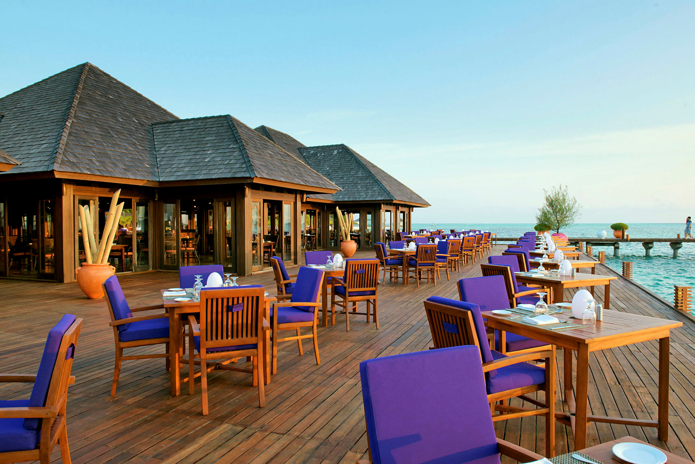 En udendørs restaurant med trægulv og borde med blå stole ved havet. (AI-genereret tekst)