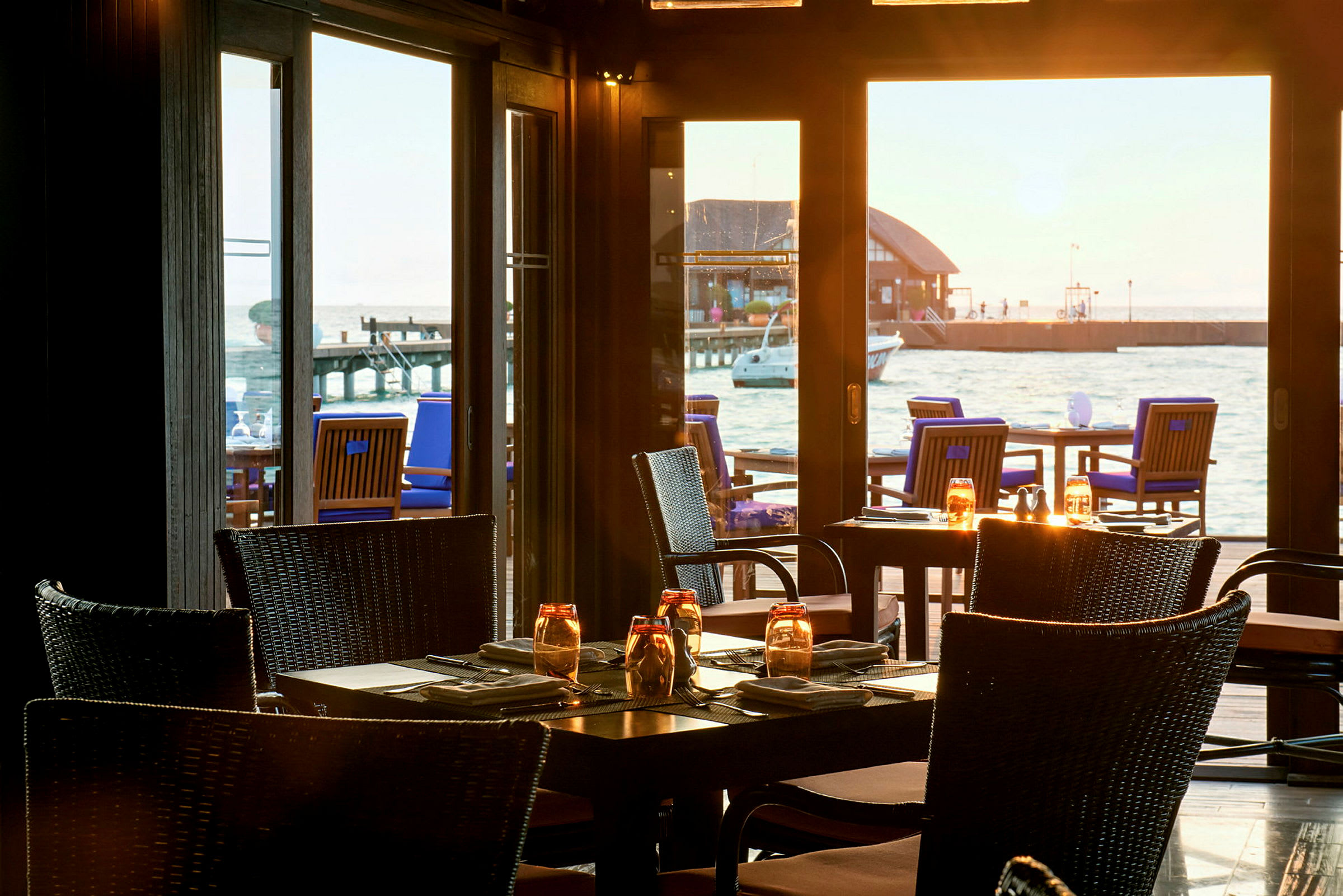 Restaurant med borde og stole indendørs samt havudsigt fra vinduer. (AI-genereret tekst)