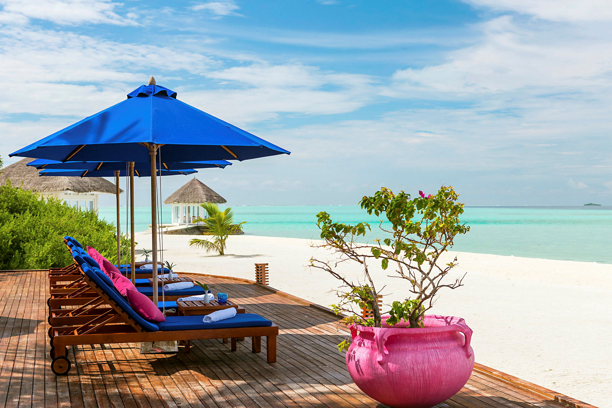 Træterrasse med liggestole og parasoller ved stranden med havet i baggrunden. (AI-genereret tekst)