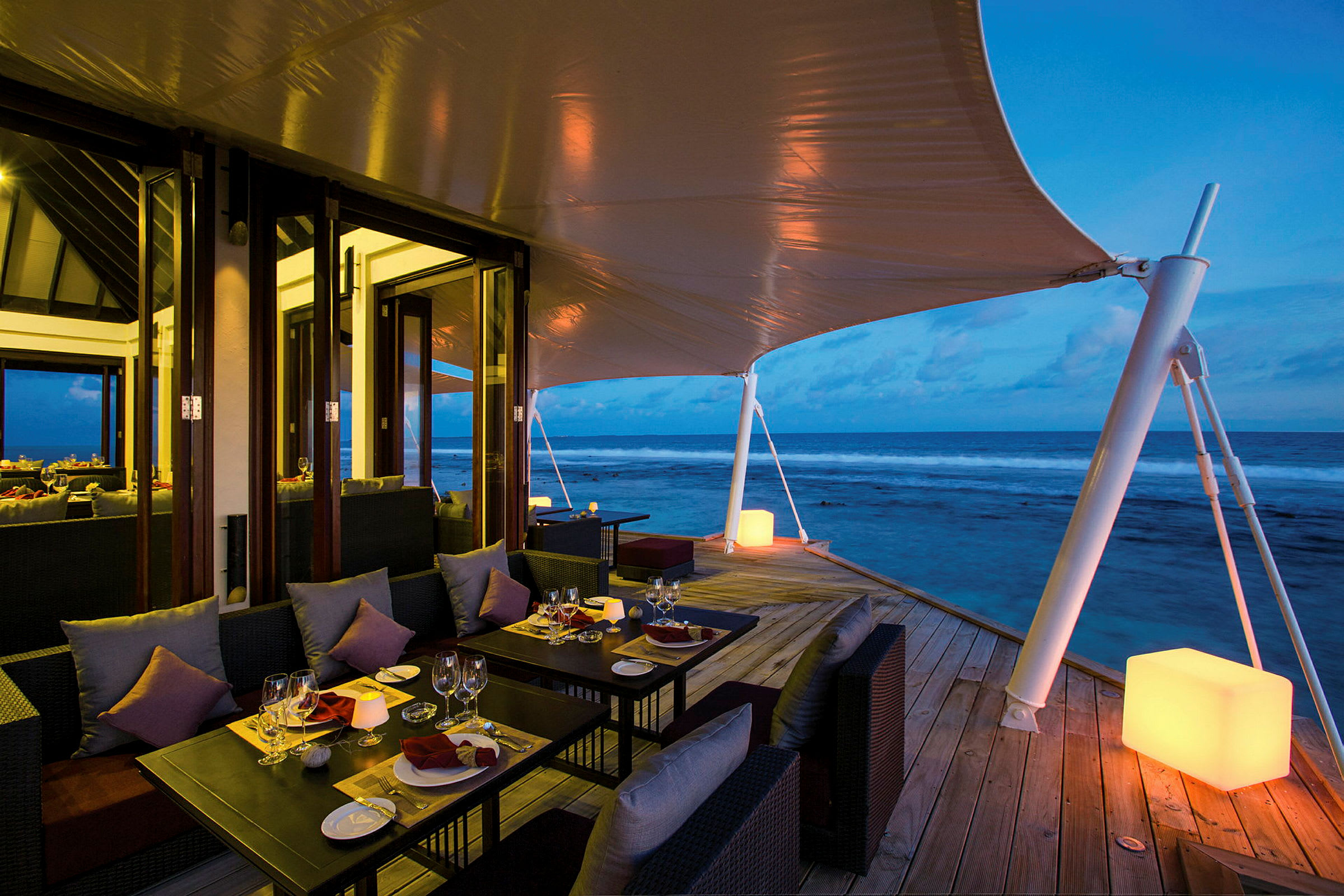 Terrasse med spiseborde og sofaer ved havet om aftenen. (AI-genereret tekst)