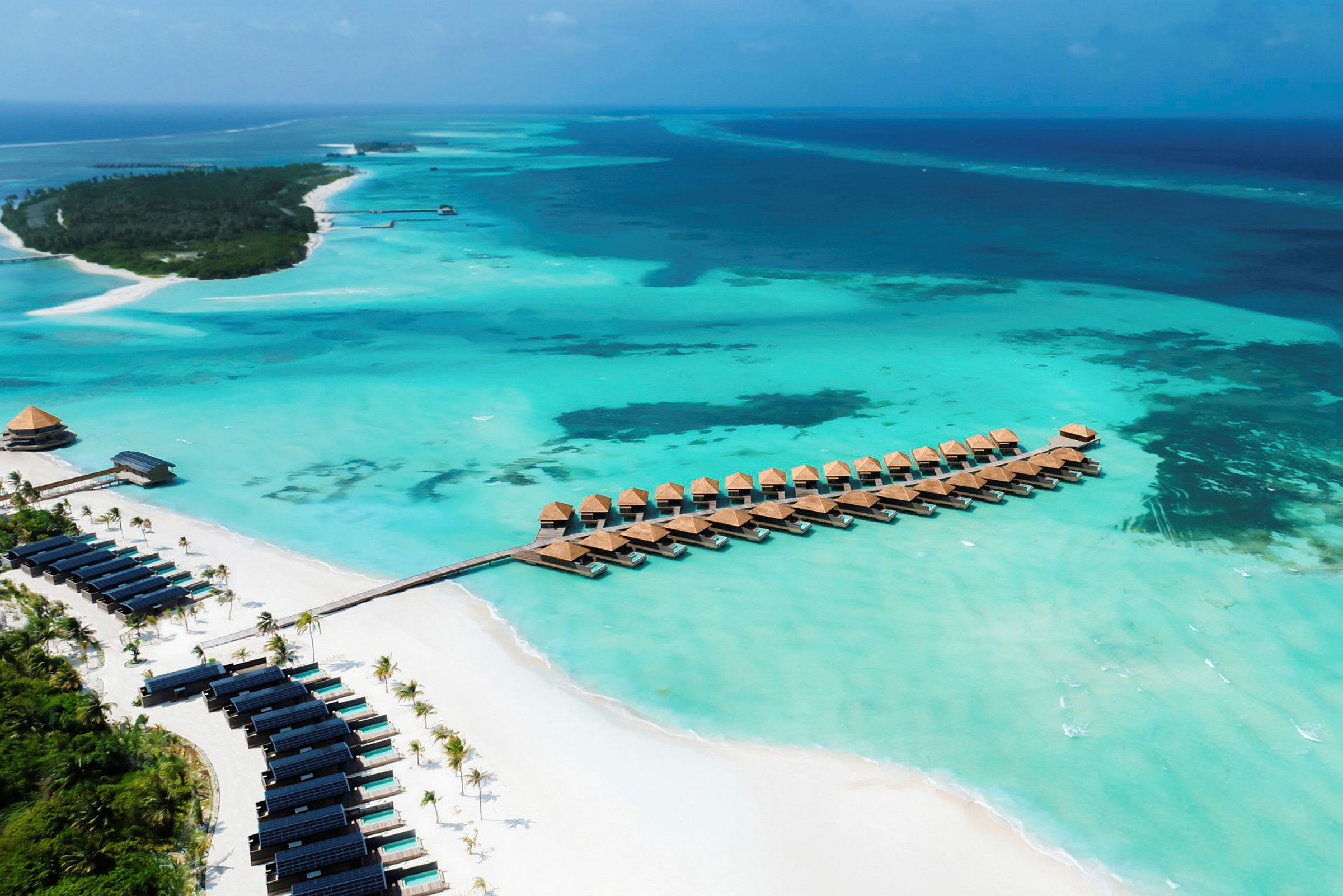 Panoramaudsigt over turkisblåt vand med bungalows på pæle og en sandstrand. (AI-genereret tekst)