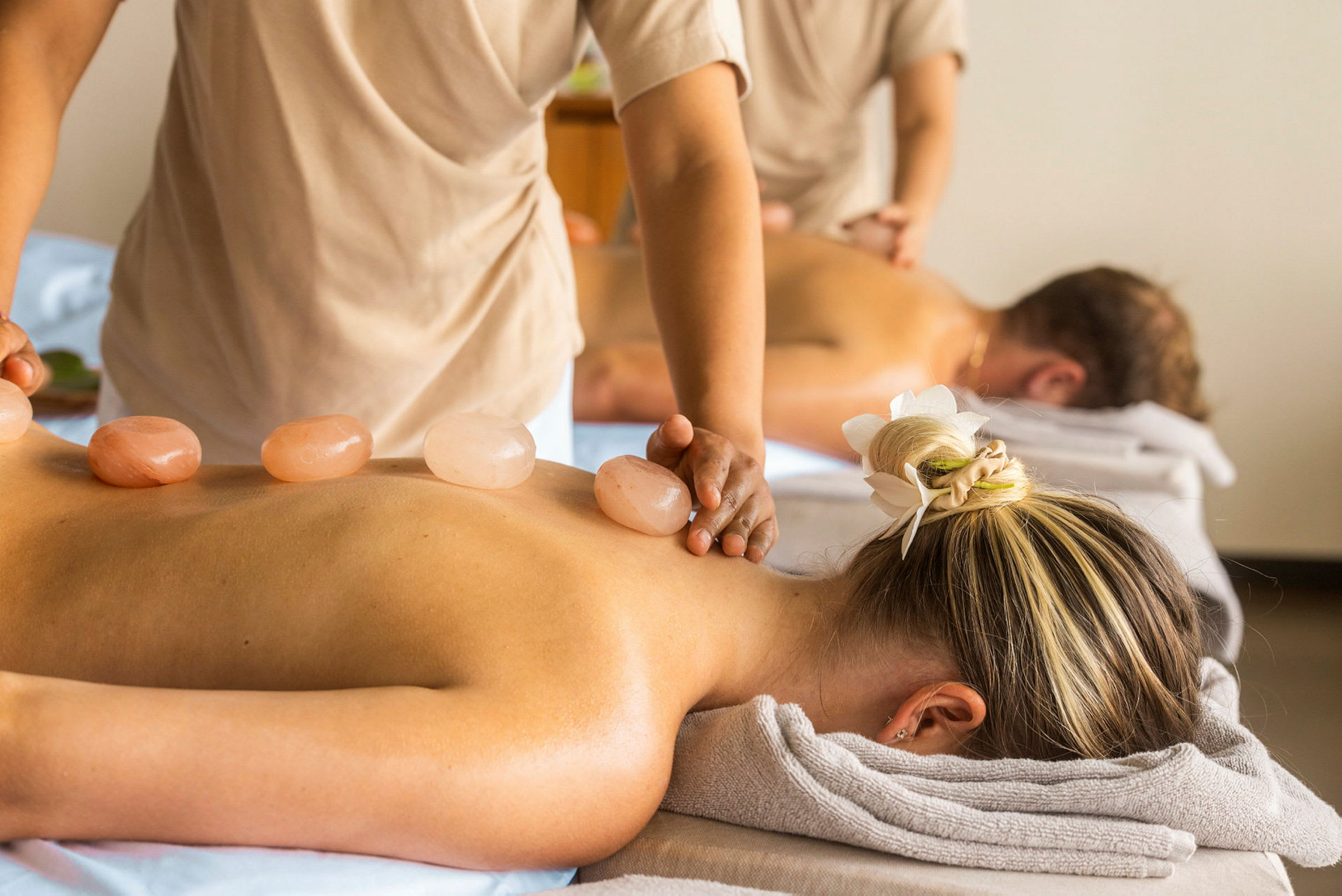 Personer nyder en massagebehandling på et spa-sted med varme sten placeret på kroppen. (AI-genereret tekst)