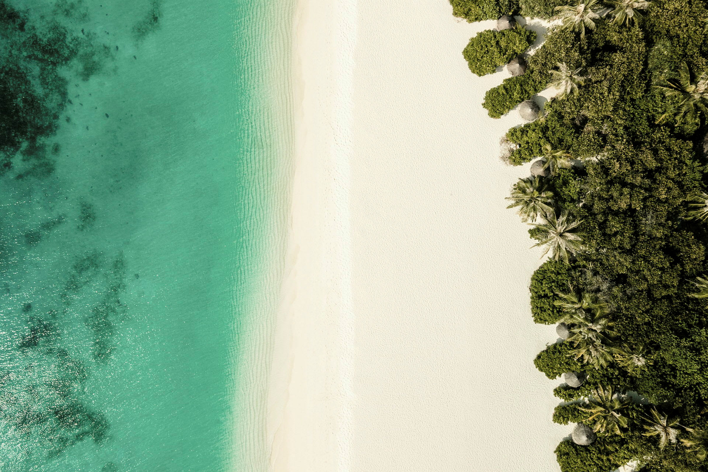 Luftfoto af en strand med hvidt sand og turkisblåt hav, omgivet af frodig vegetation. (AI-genereret tekst)