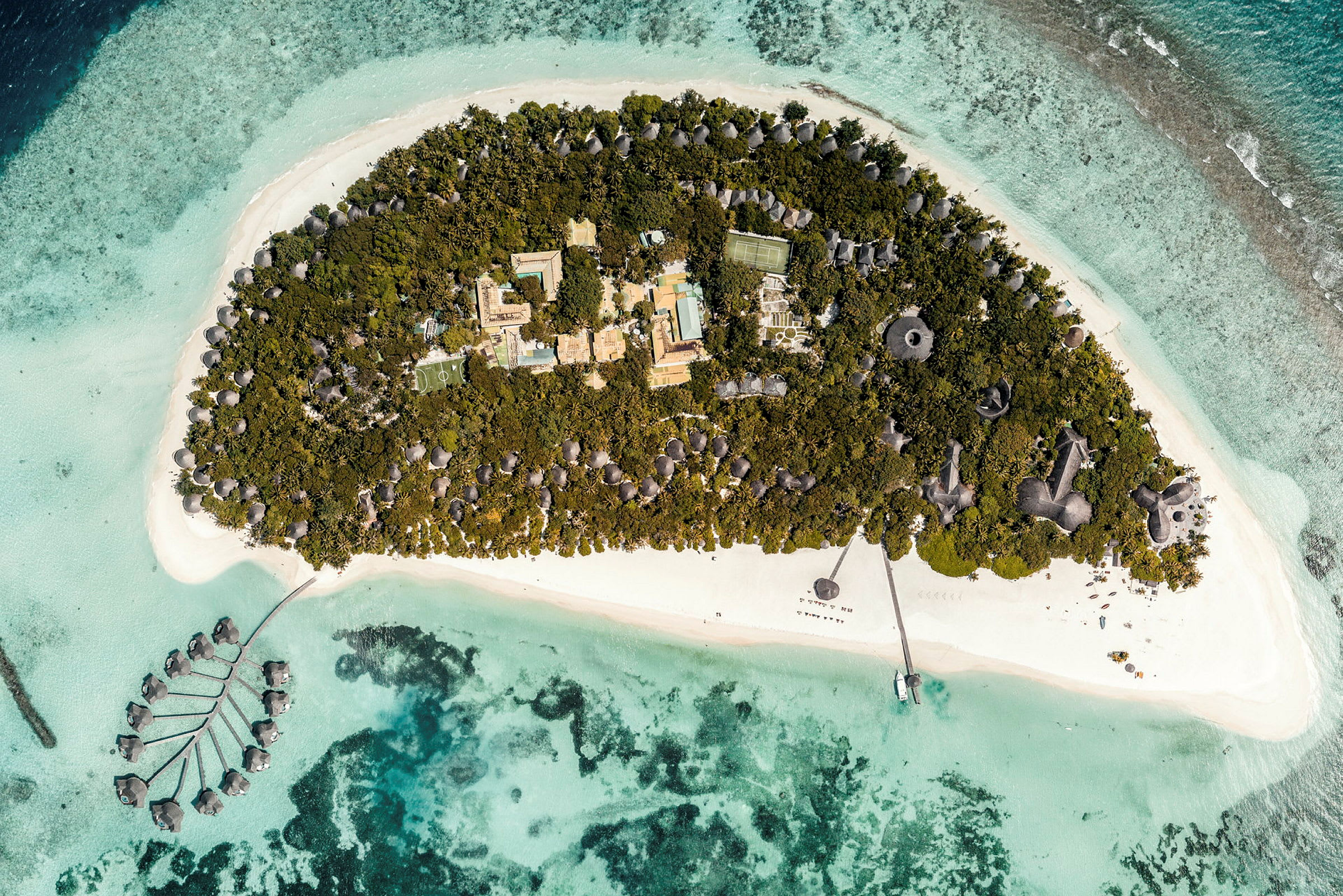 Luftfoto af en tropisk ø omgivet af turkisblåt vand og resort i grøn vegetation. (AI-genereret tekst)