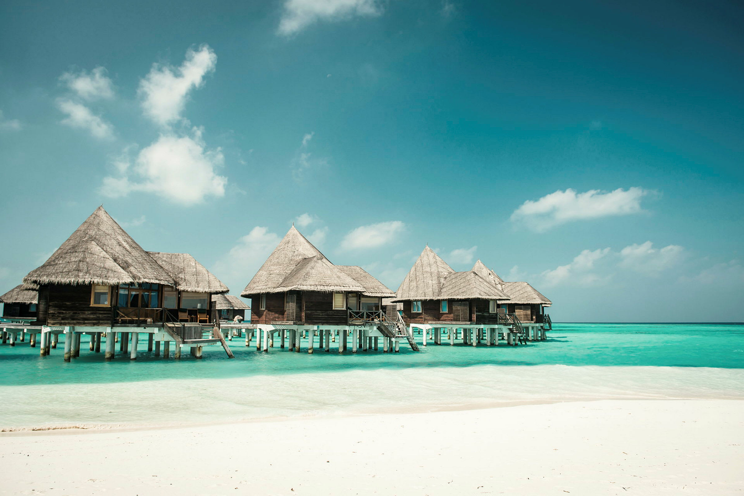 Bungalows på pæle over blåt vand ved en strand. (AI-genereret tekst)