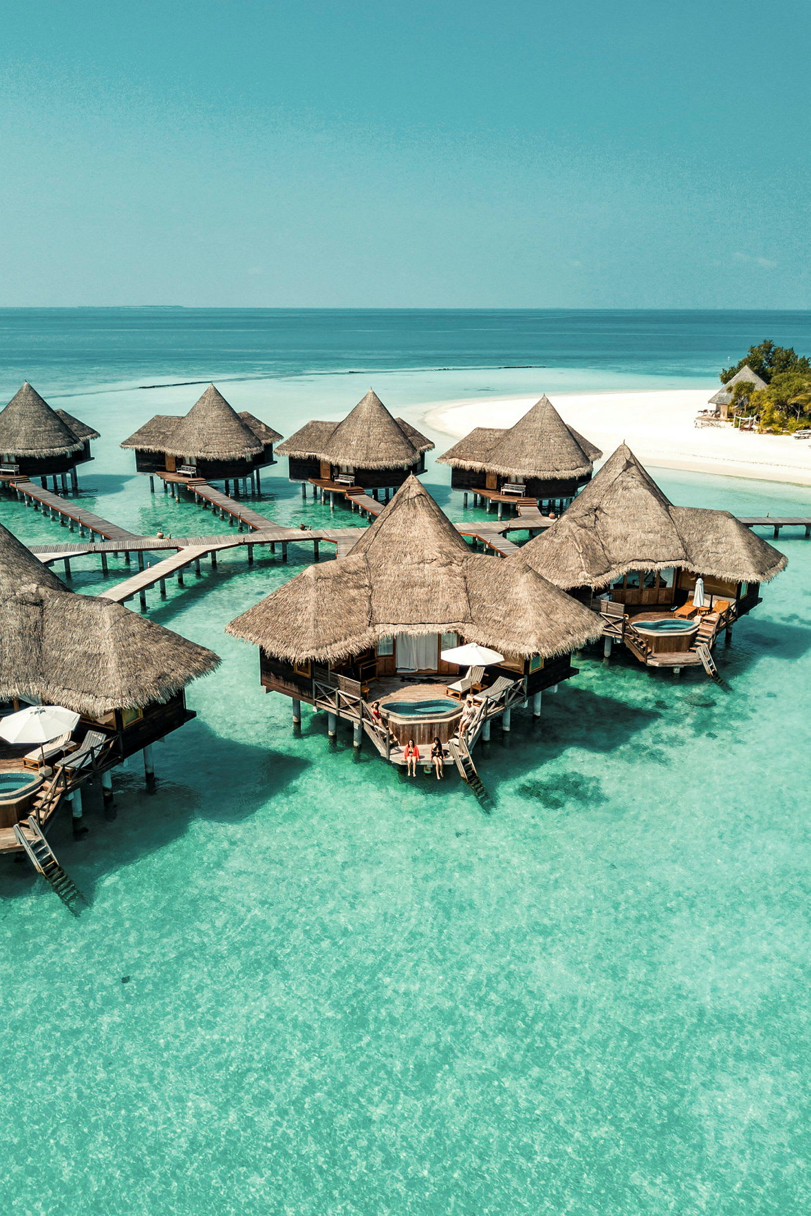 Bungalows på pæle over turkis vand ved en hvid sandstrand. (AI-genereret tekst)